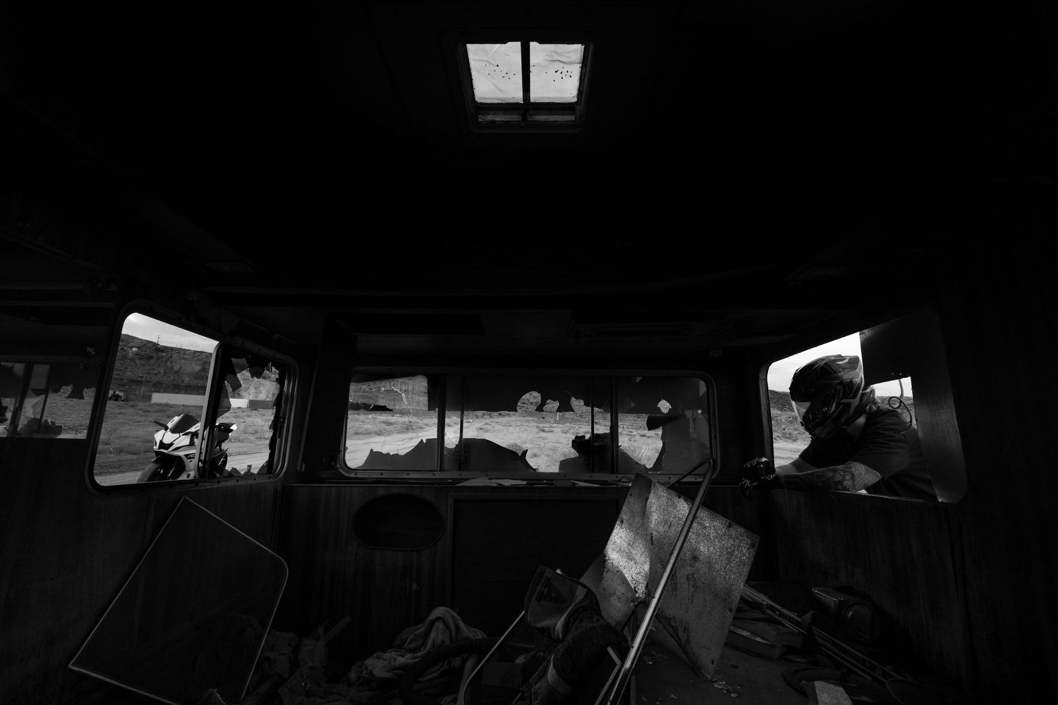 Black and white interior view of an old abandoned bus with broken windows revealing a dark landscape outside.