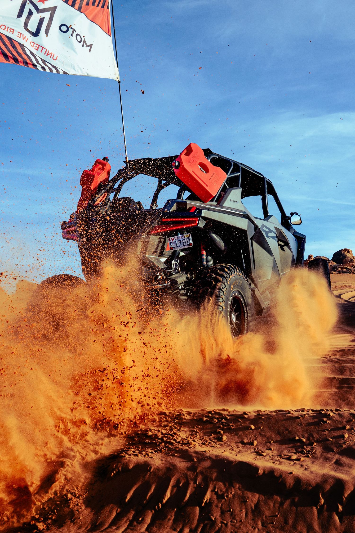 Can-Am UTV kicking up dramatic orange dirt and dust clouds on a rugged off-road trail.
