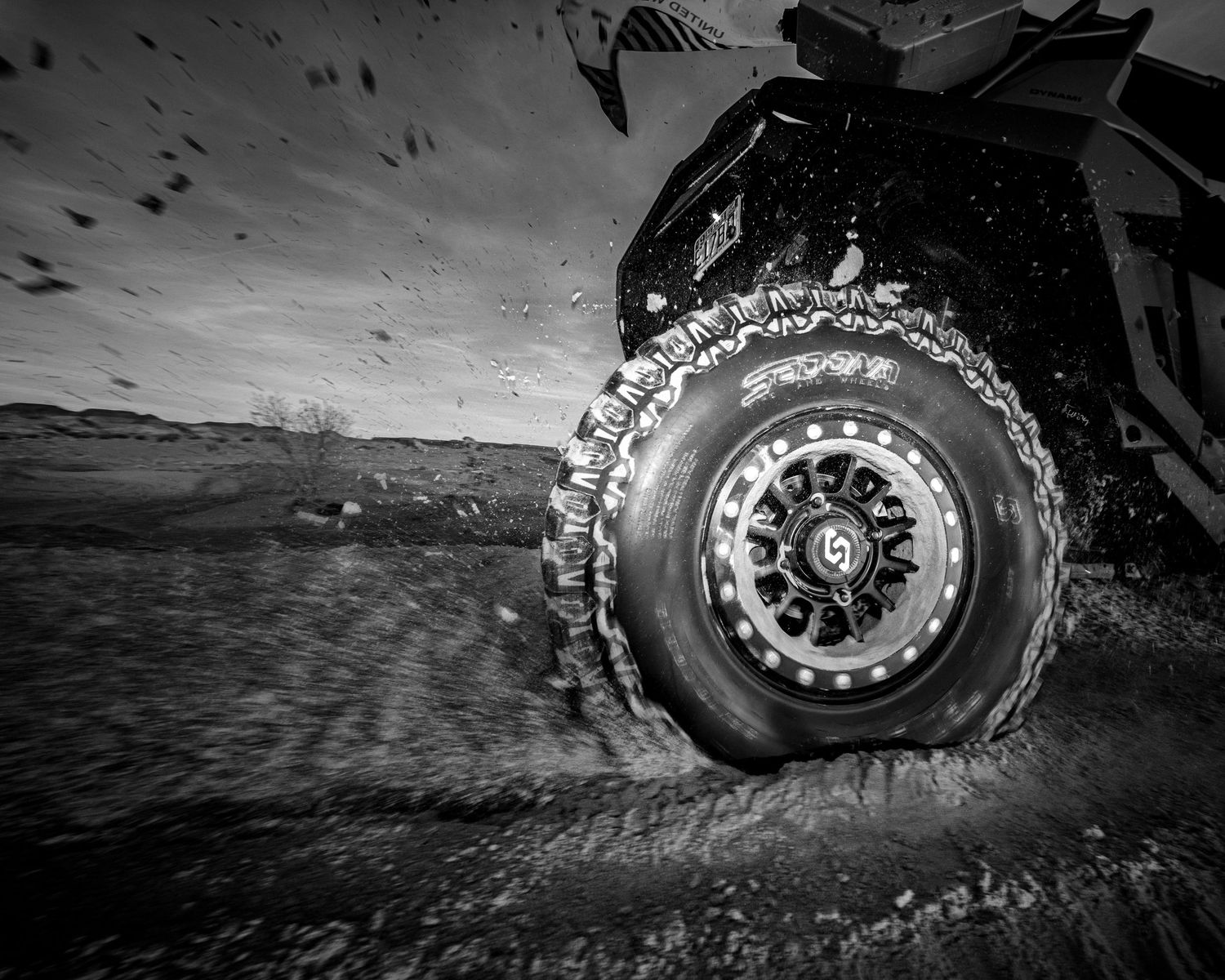 Black and white close-up of spinning UTV wheel with mud splatter on beadlock rim.