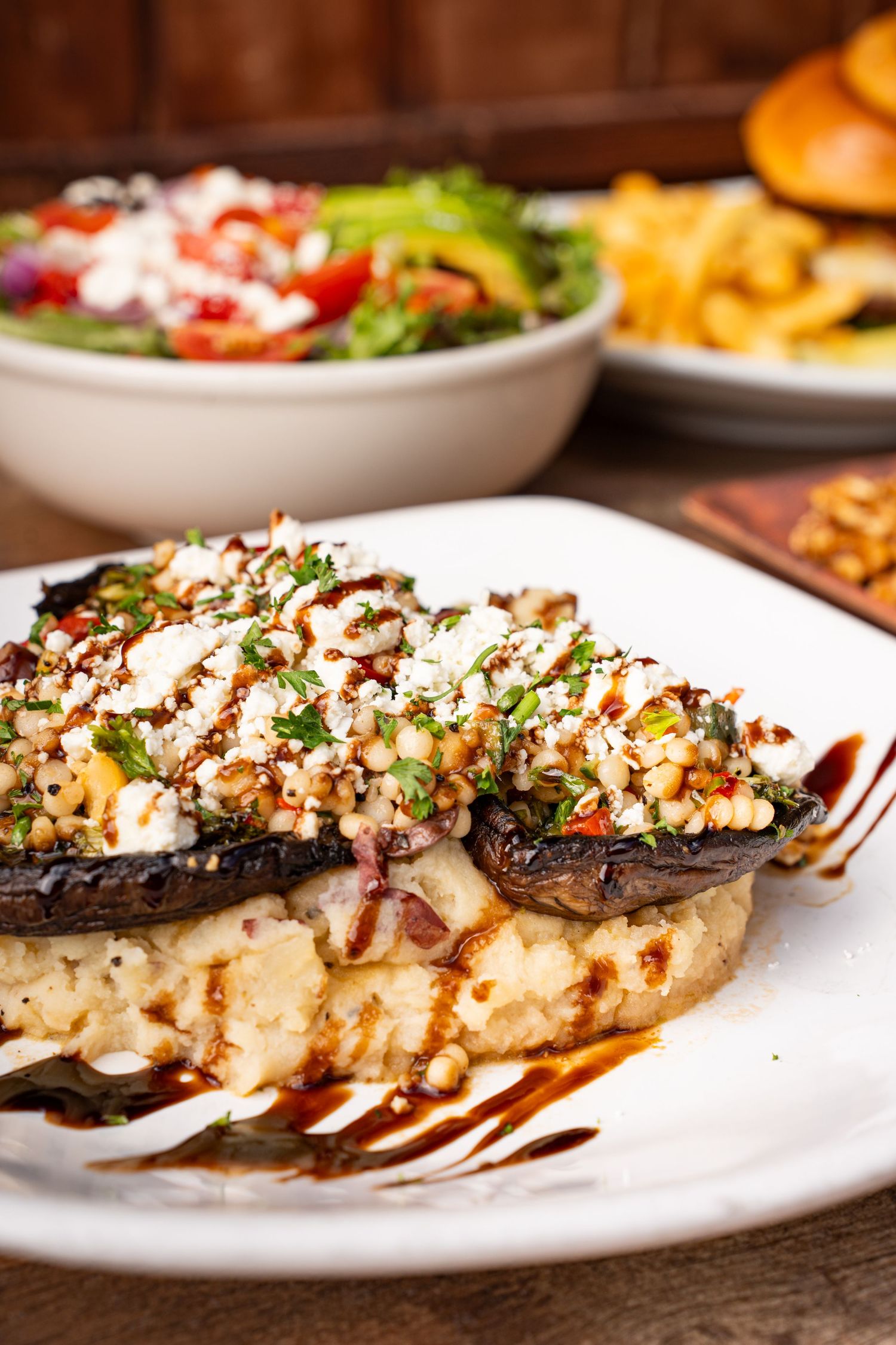 Grilled portobello mushroom on creamy polenta topped with crumbled feta, herbs, and balsamic drizzle on white plate.