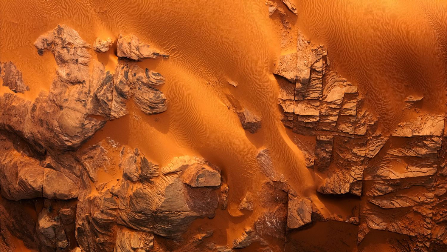 Aerial view of dramatic orange rocky desert landscape with deep shadows and textured formations.