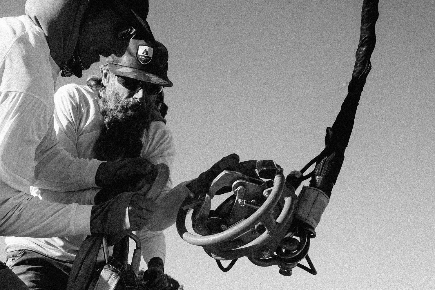 Black and white photo of two workers in hard hats examining heavy industrial equipment outdoors.