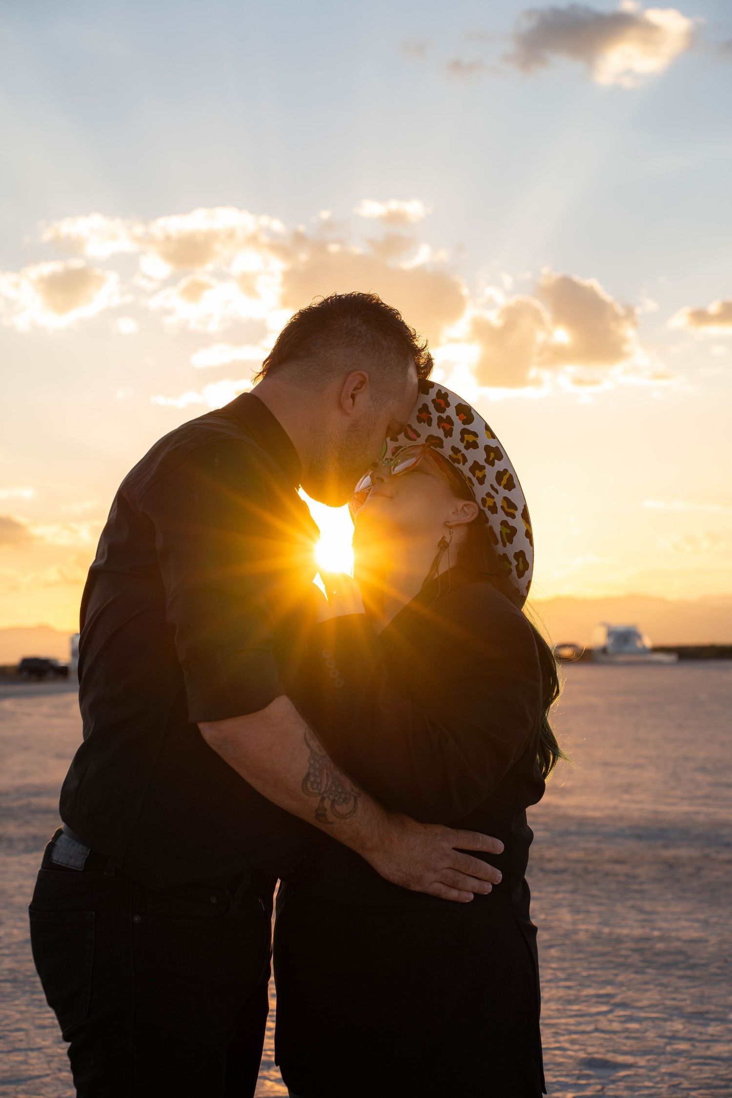 Couple sharing a kiss silhouetted against a stunning golden sunset with lens flare.