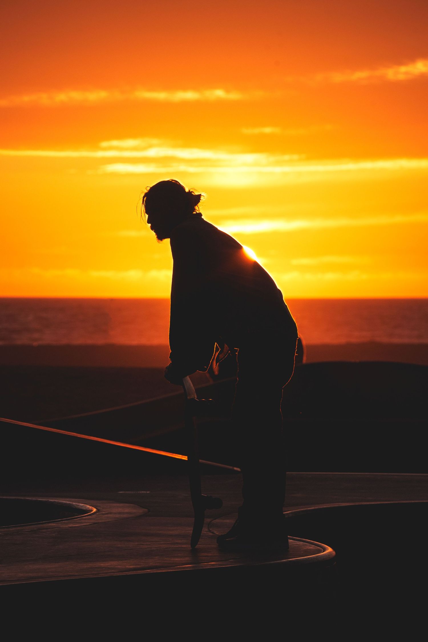 Silhouette of a worker holding a hose against a vibrant orange ocean sunset.
