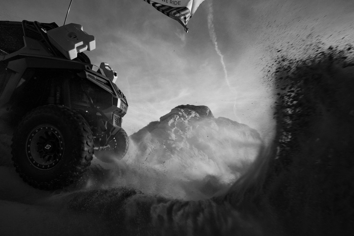 Black and white dramatic shot of an off-road UTV churning through sandy terrain.
