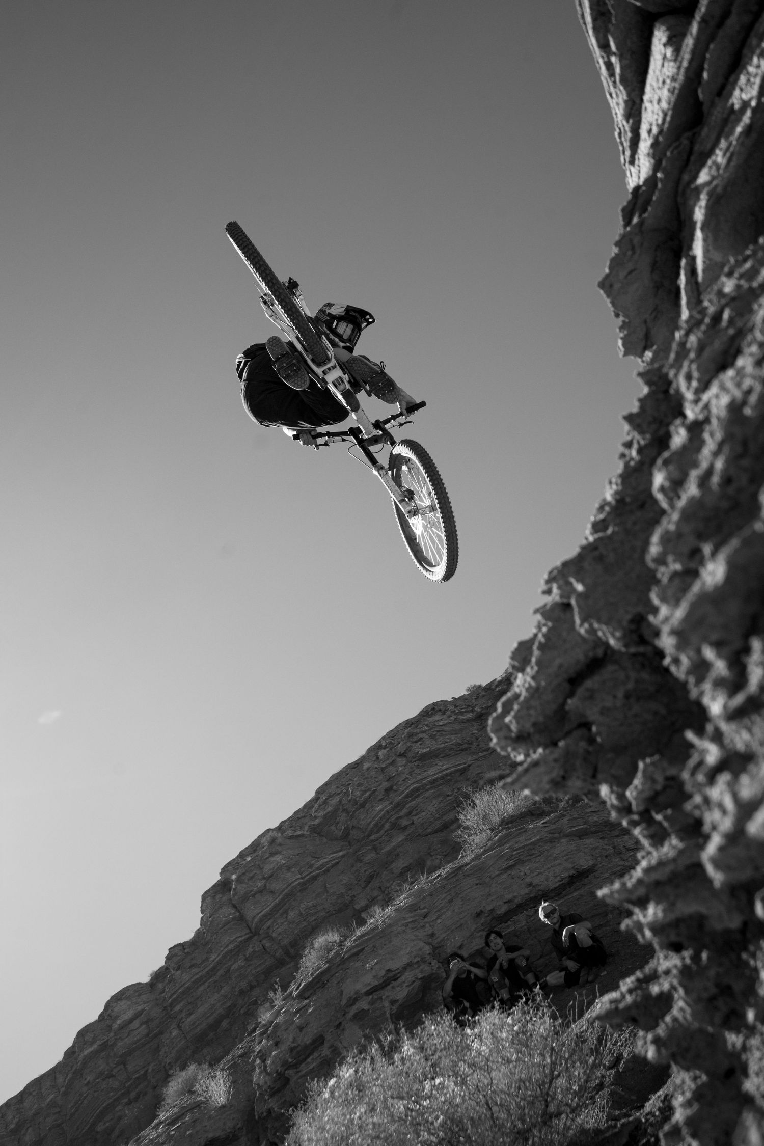Black and white shot of mountain biker performing aerial trick off rocky cliff edge.