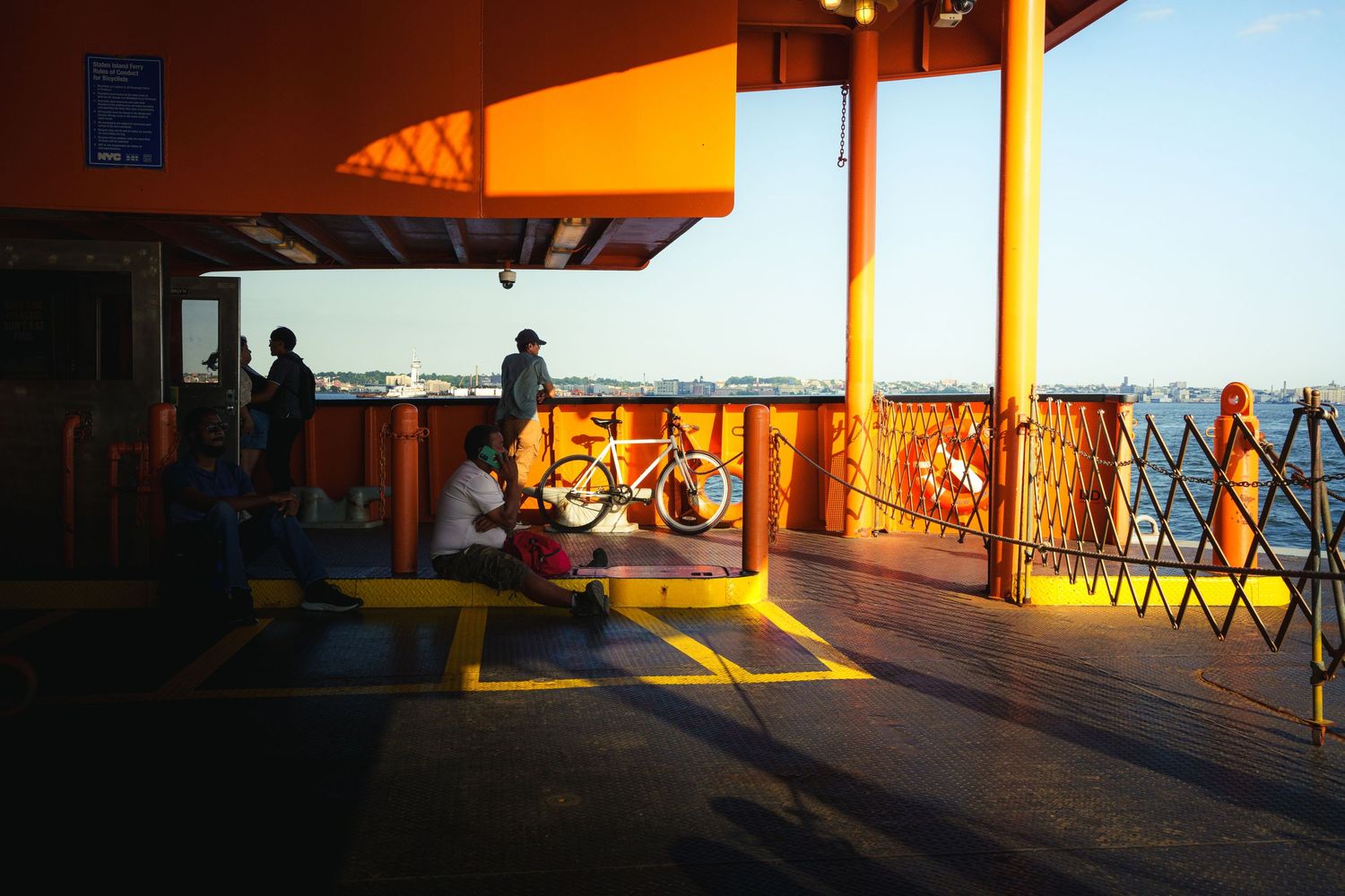 Person sitting with a yellow bicycle on a vibrant orange ferry deck at golden hour by the sea.