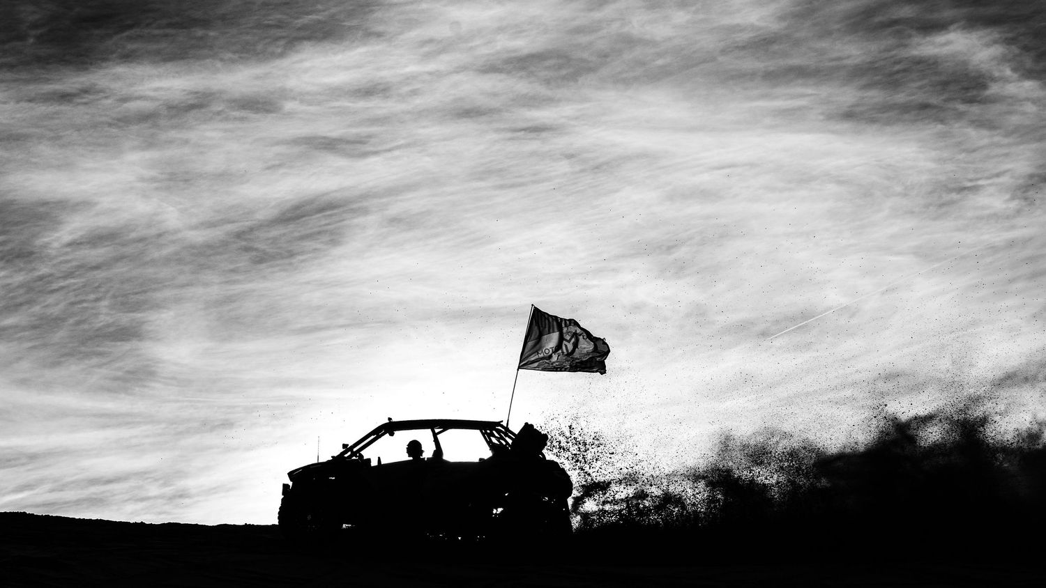 Silhouette of UTV with waving flag against dramatic cloudy black and white sky.