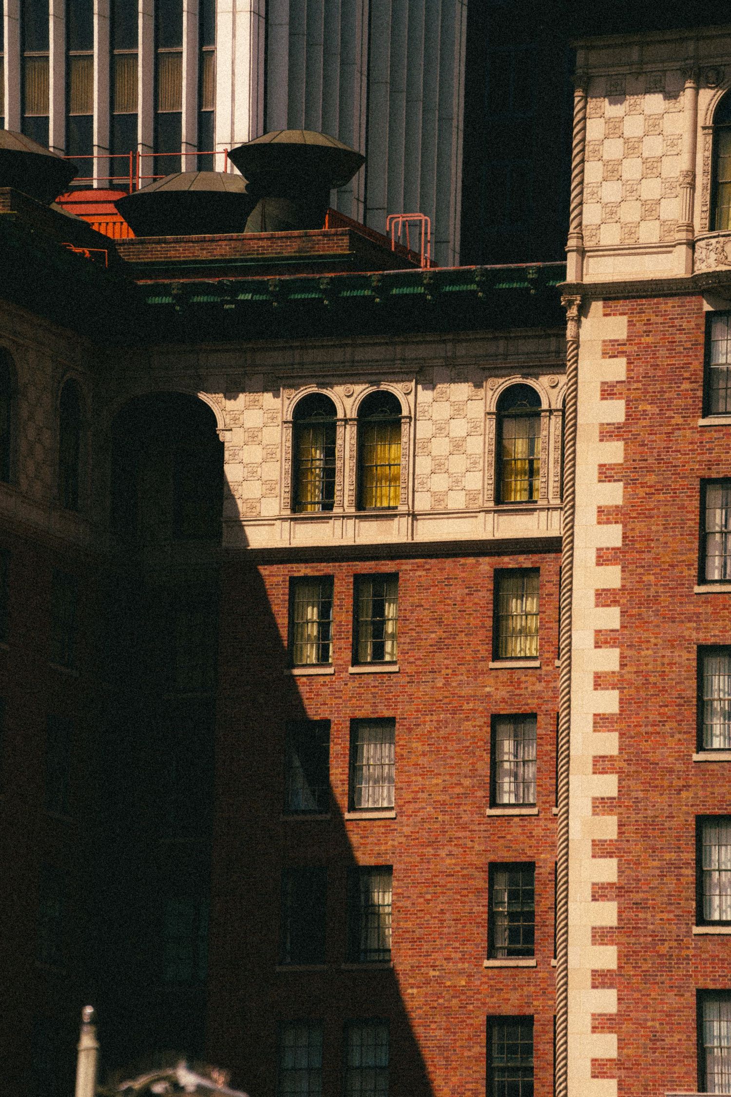 Sunlit red brick building with arched windows and ornate details in a dense urban cityscape.