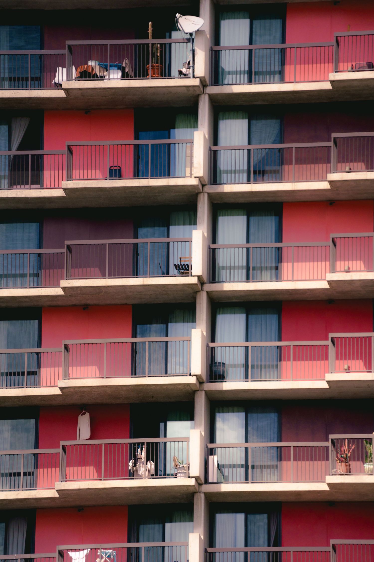 Colorful pink and red balconies on a modern residential apartment building facade in bright sunlight.