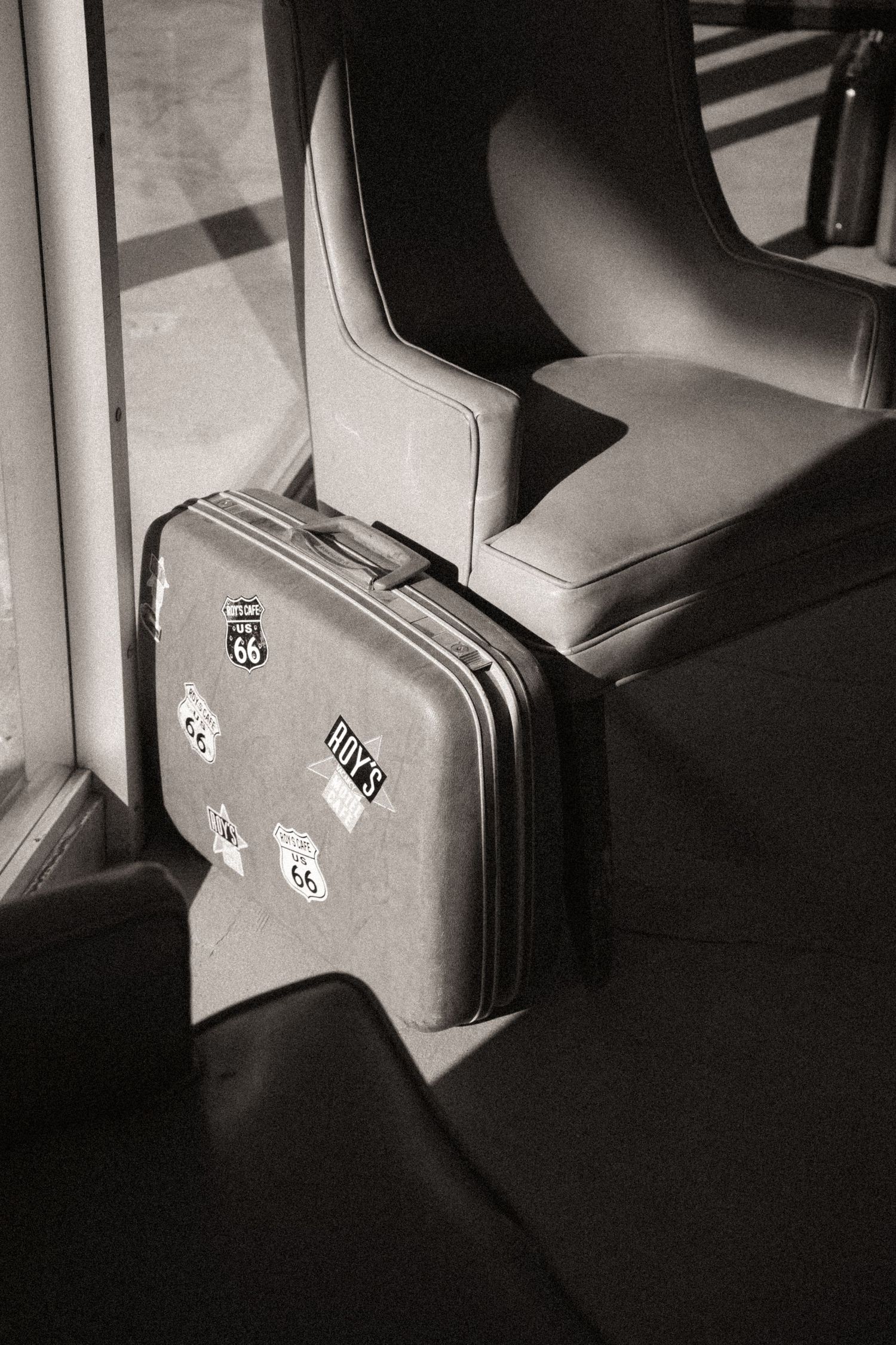 Vintage suitcase with Route 66 stickers beside a seat in black and white.