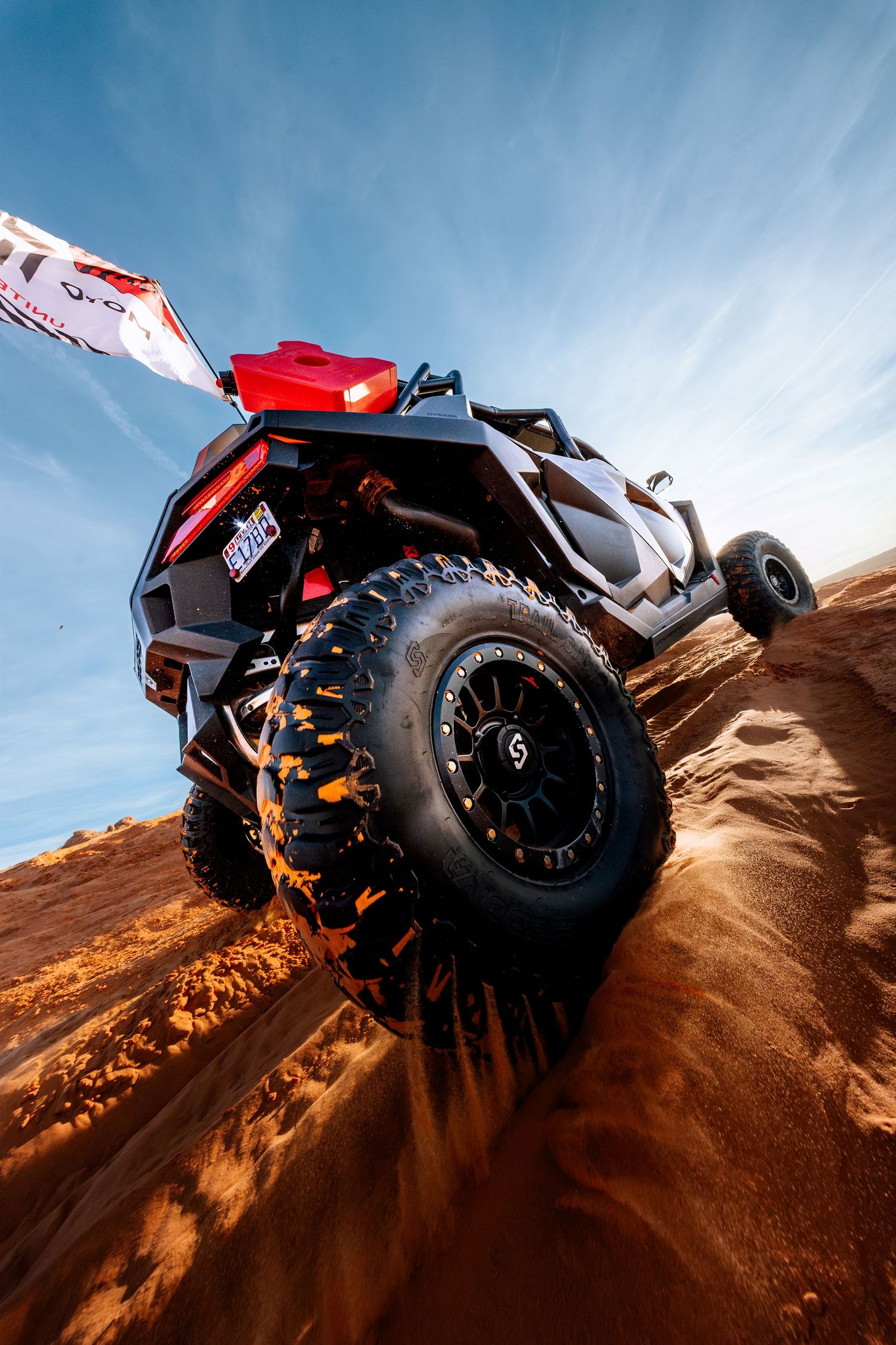 Low angle view of UTV climbing red sand dunes with aggressive off-road tires under blue sky.