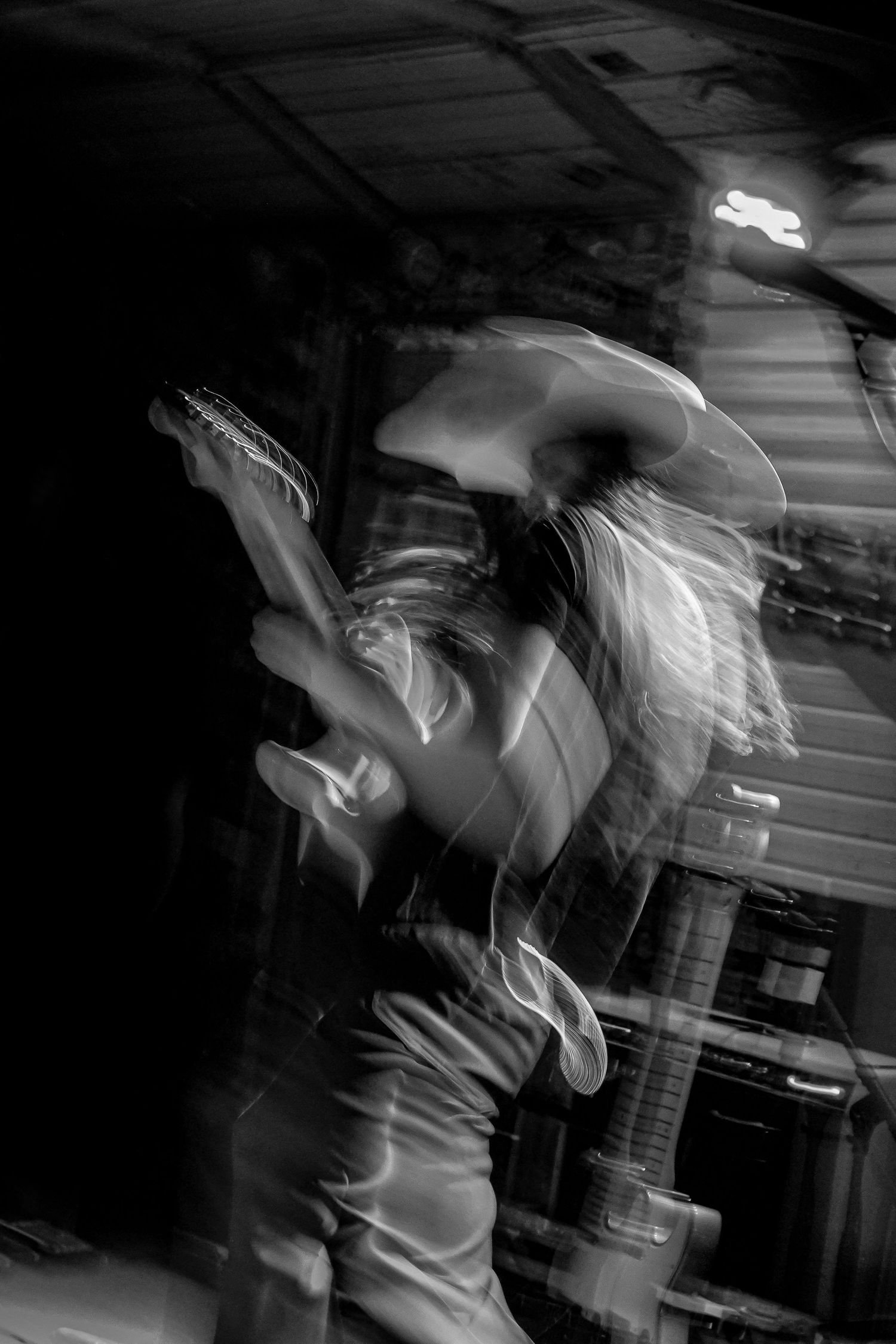 Motion blur black and white photo of energetic guitarist performing on stage with cowboy hat.