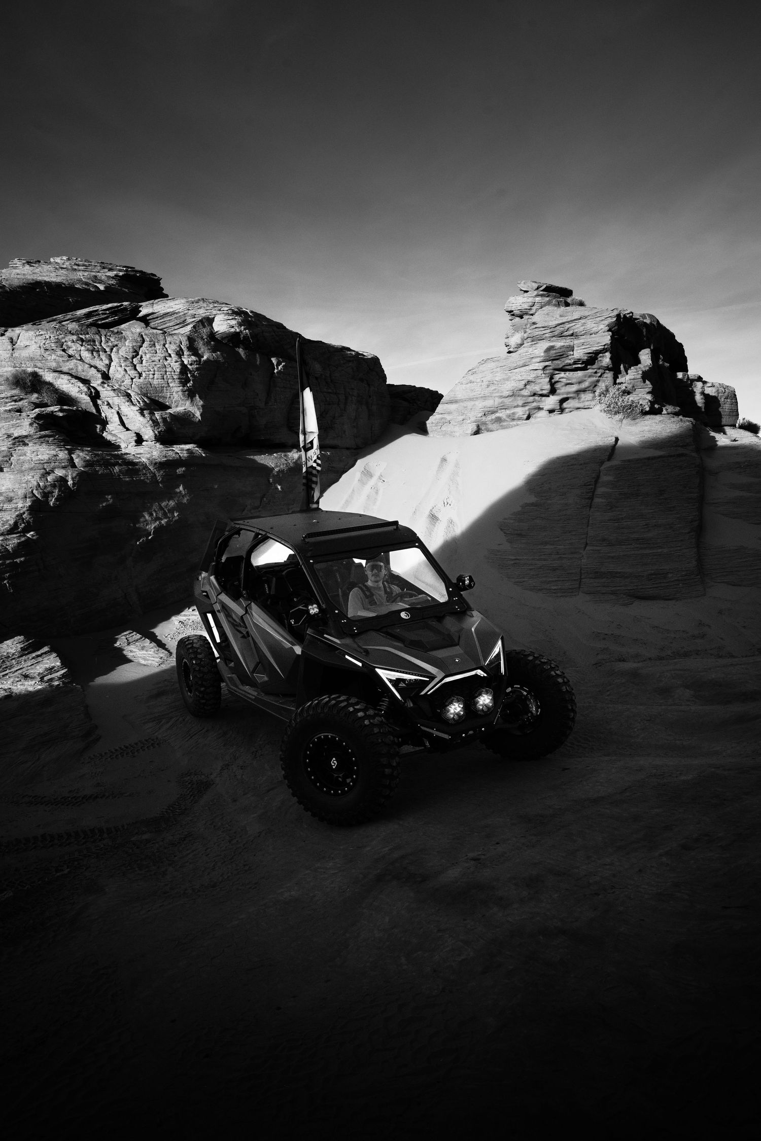 Black and white UTV parked on desert rock formations with towering sandstone cliffs background.