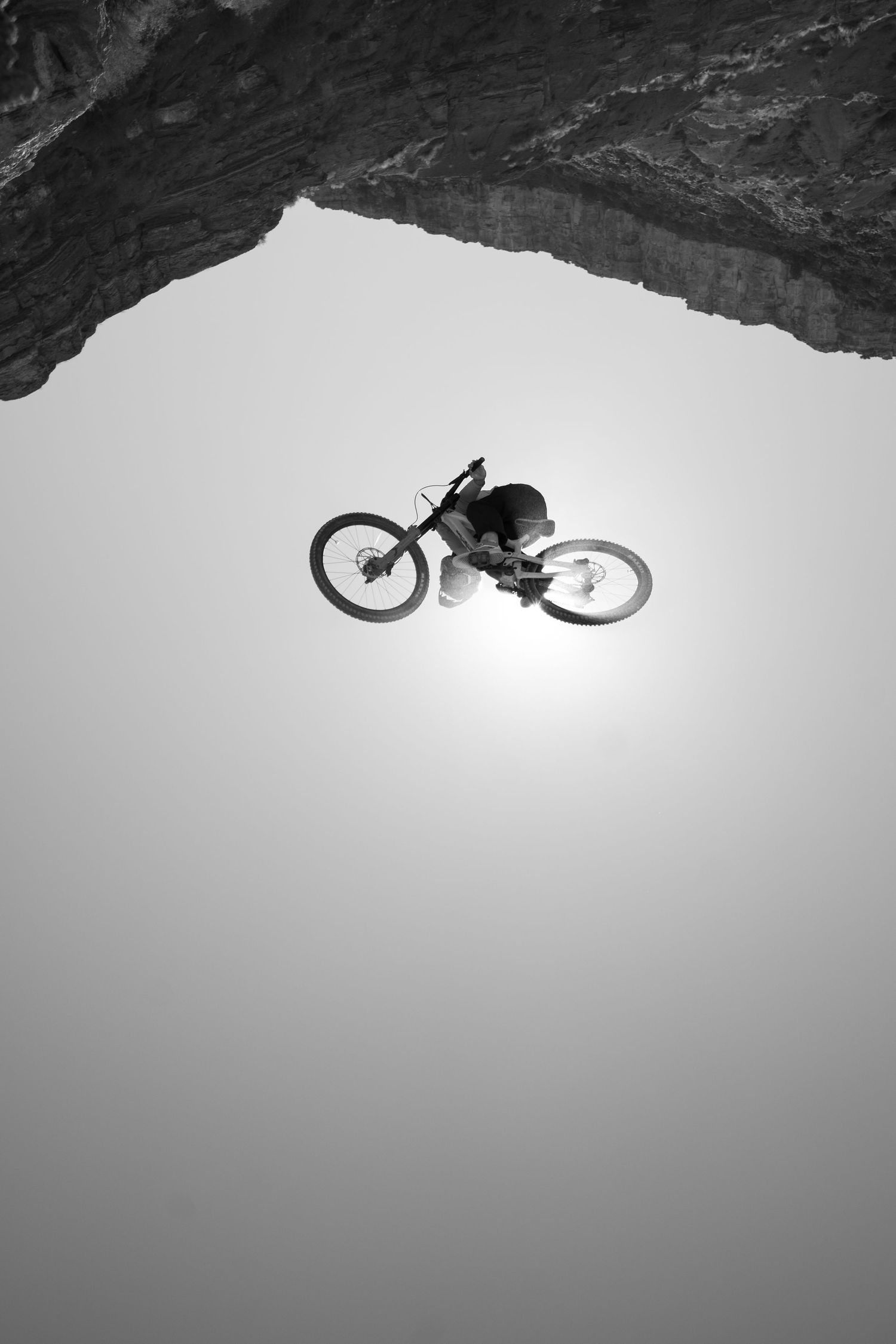 Black and white photo of a mountain biker jumping off a rocky cliff edge.