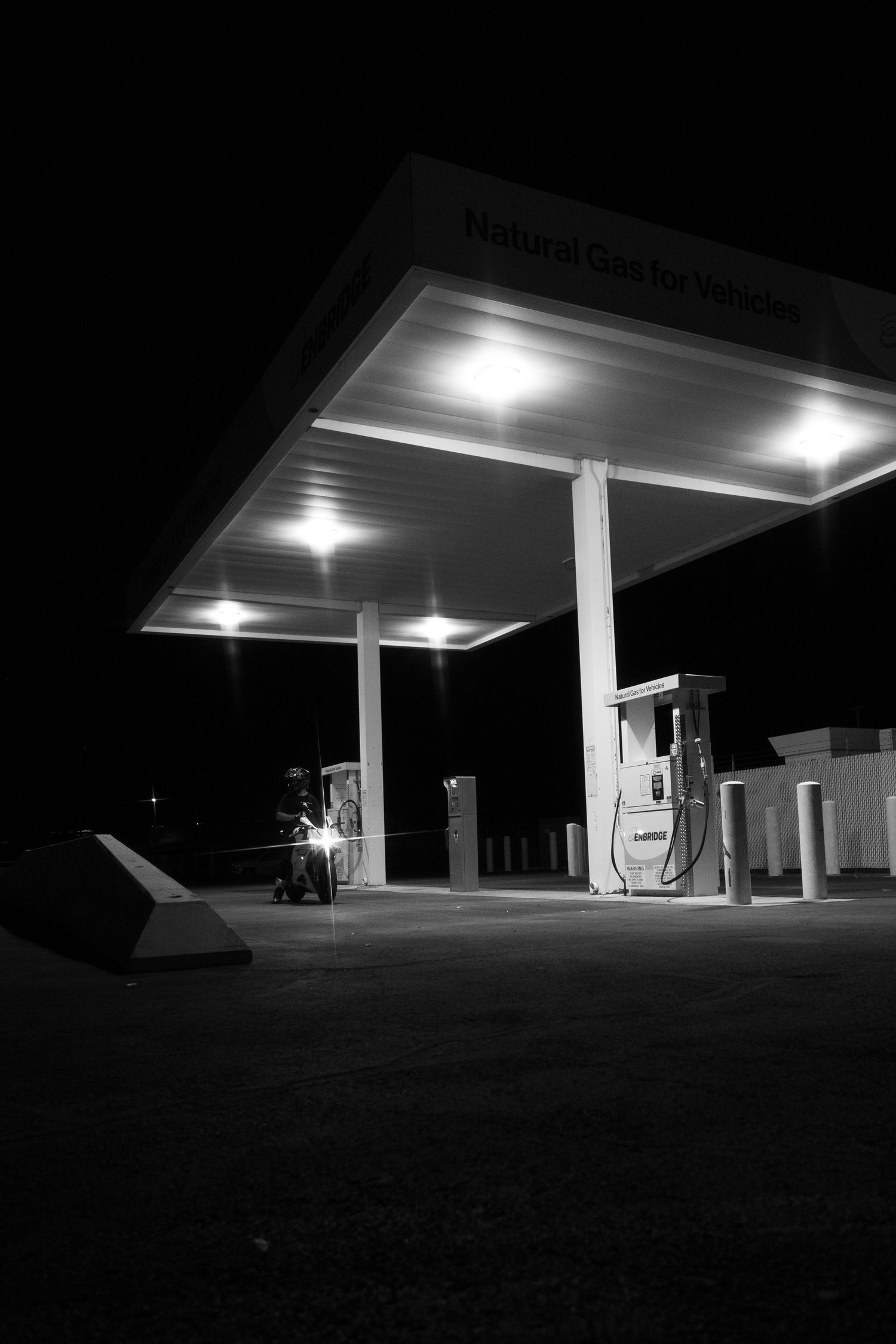 Empty natural gas vehicle fueling station illuminated at night in black and white photography.
