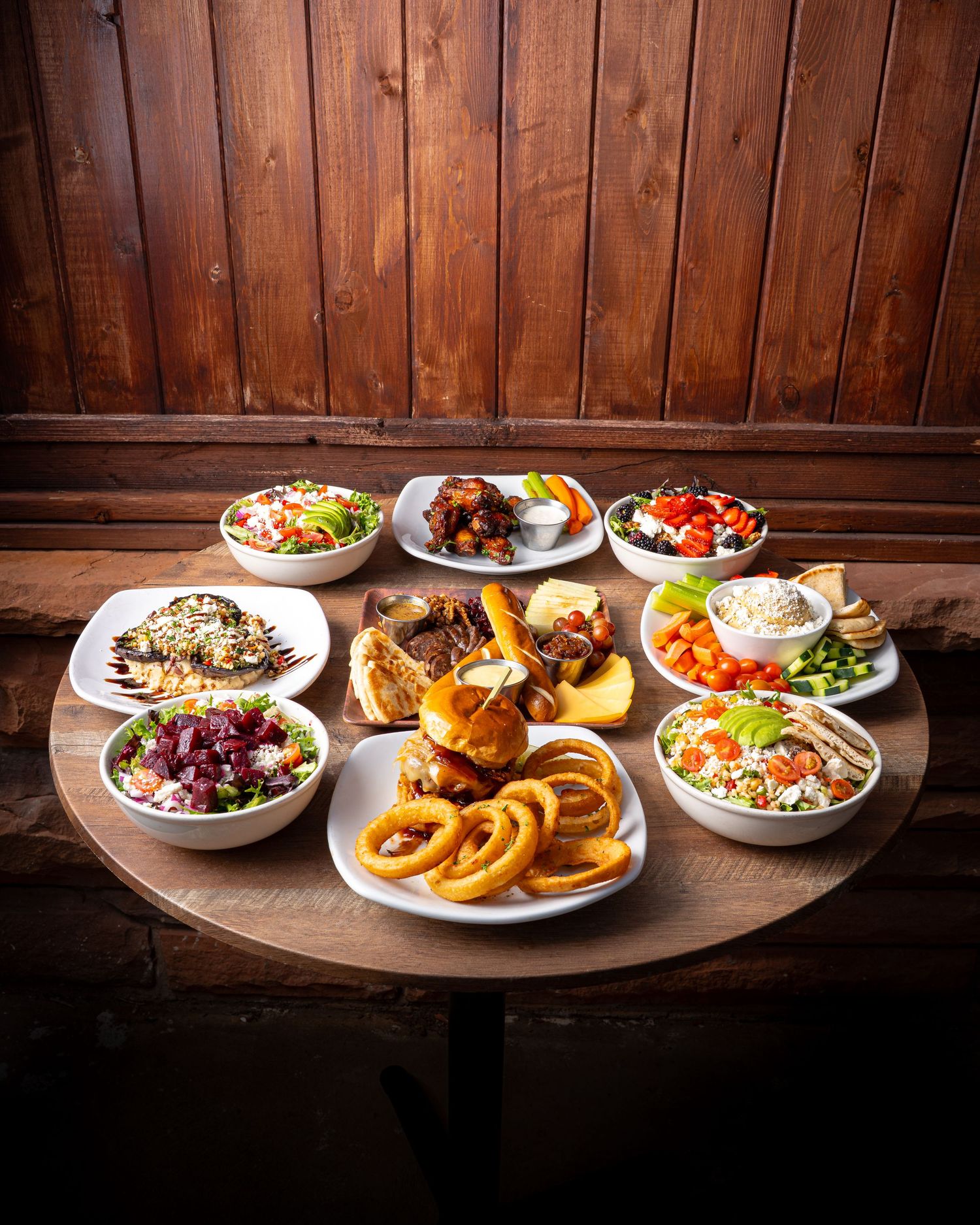 Overhead view of multiple bowls of food and onion rings arranged on a round wooden table.