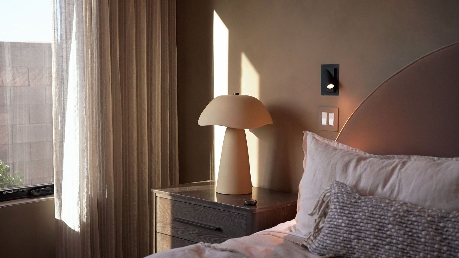 Cozy bedroom with mushroom lamp on nightstand in warm sunlight.