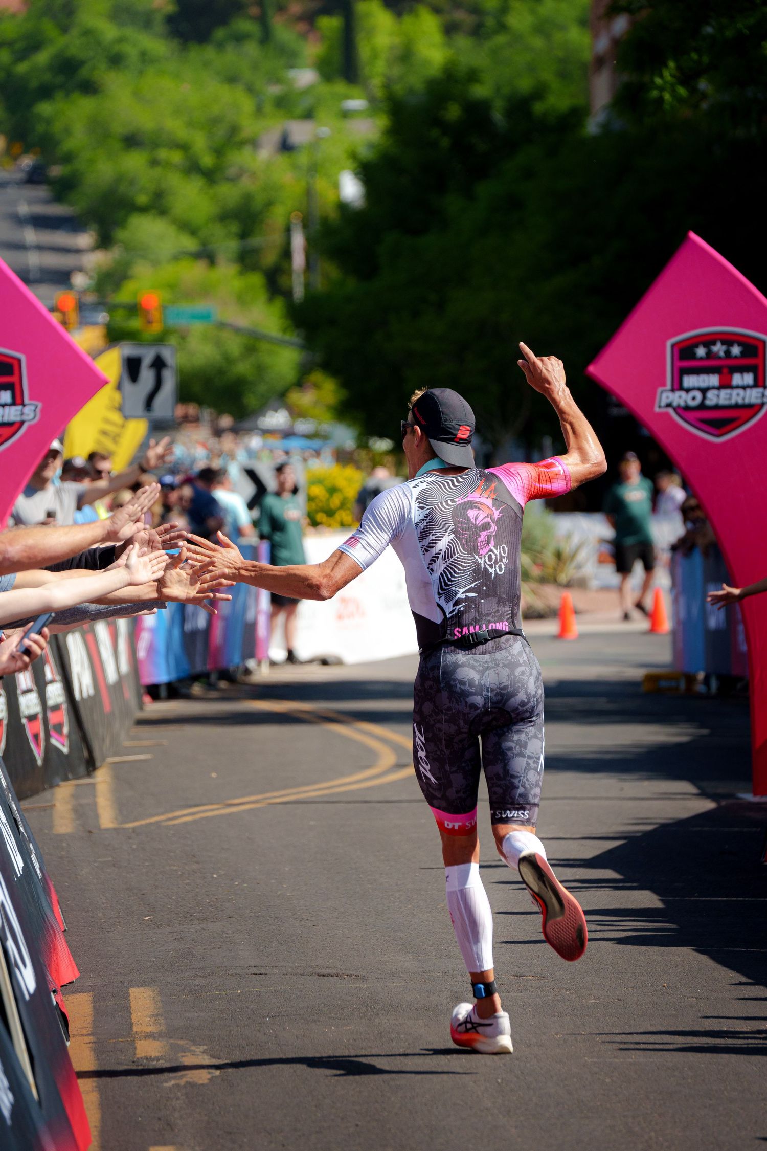 Triathlete in pink and white kit runs along spectator-lined finish chute giving high-fives at a triathlon event.