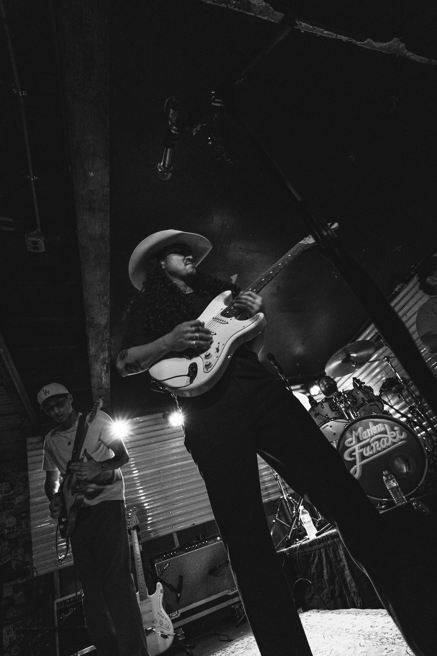Low angle black and white shot of guitarist in cowboy hat playing Fender Stratocaster on stage.