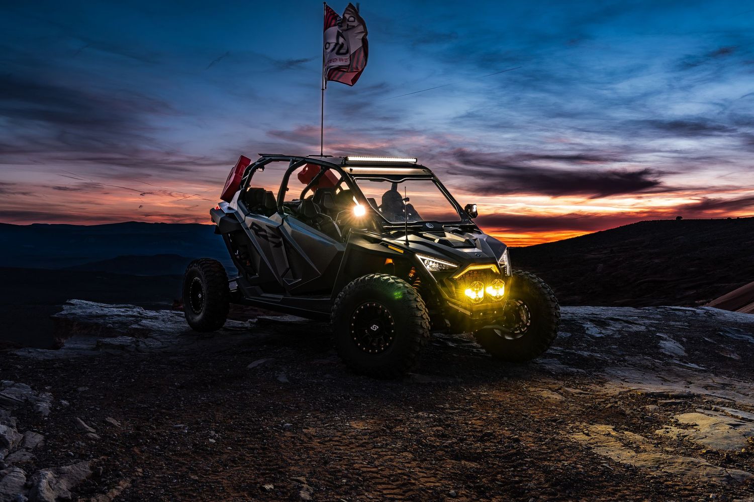UTV with glowing yellow LED lights parked on rocky overlook during vibrant sunset.