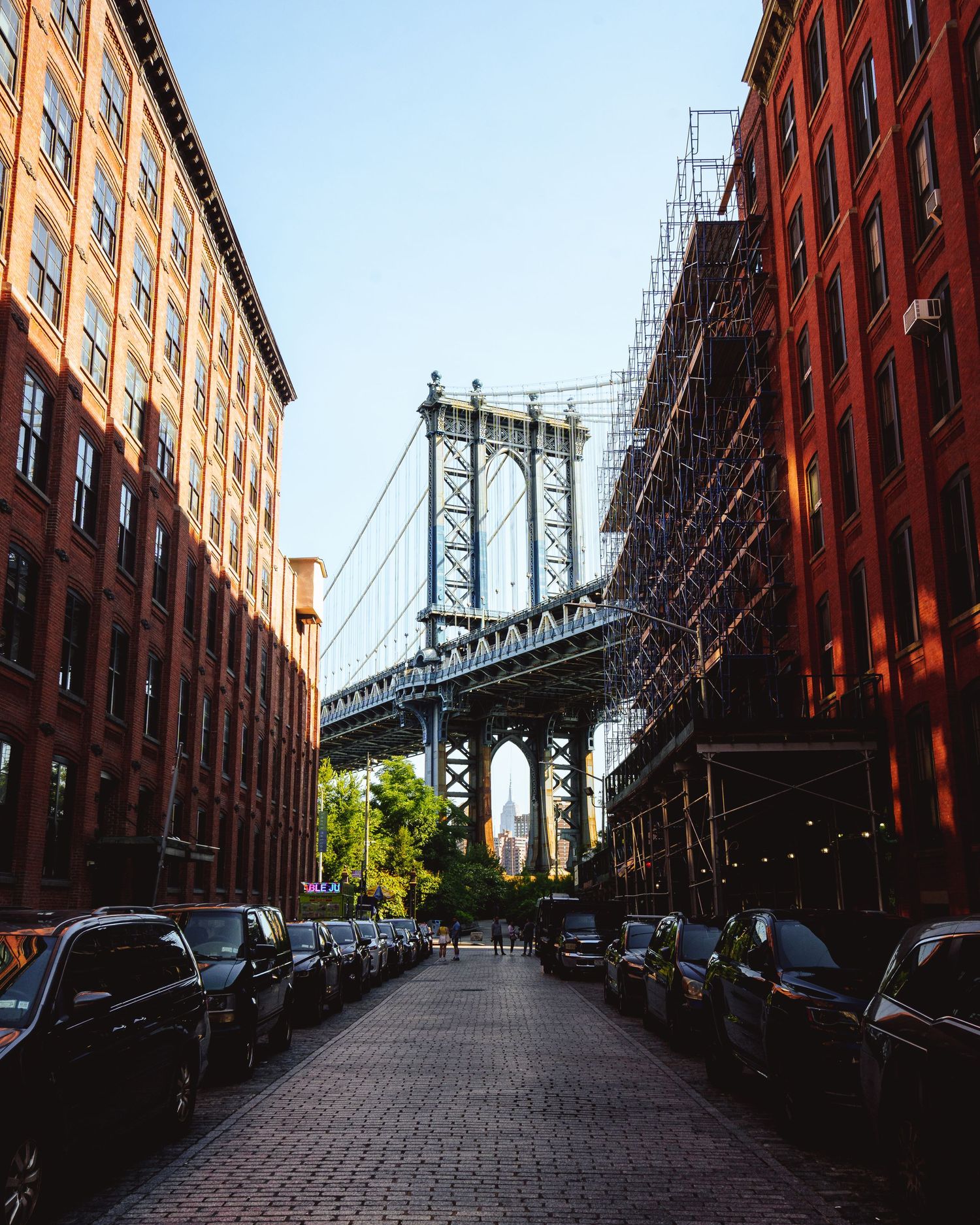 View of Manhattan Bridge framed by red brick buildings on a cobblestone street in DUMBO, Brooklyn, NYC.