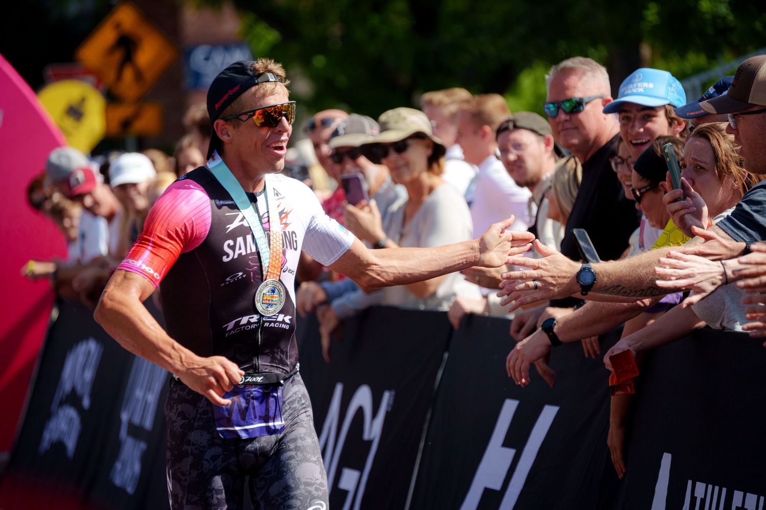 Pro triathlete Sam Long shakes hands with fans along the finish line barrier at an Ironman race.