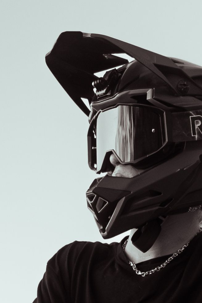 Close-up portrait of a motocross rider wearing a black helmet and reflective goggles against pale sky.