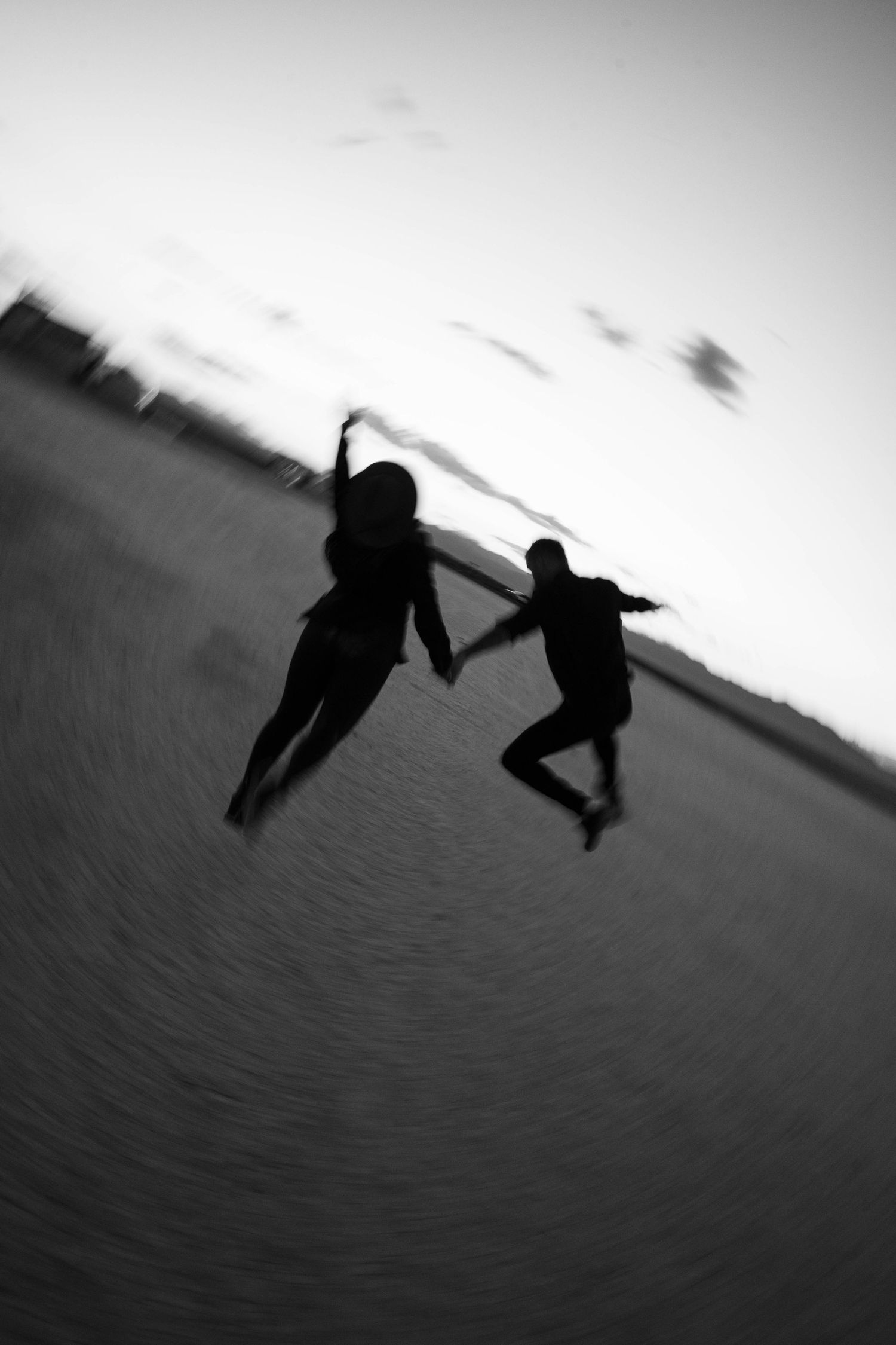 Black and white silhouette of couple jumping and holding hands on sandy desert.