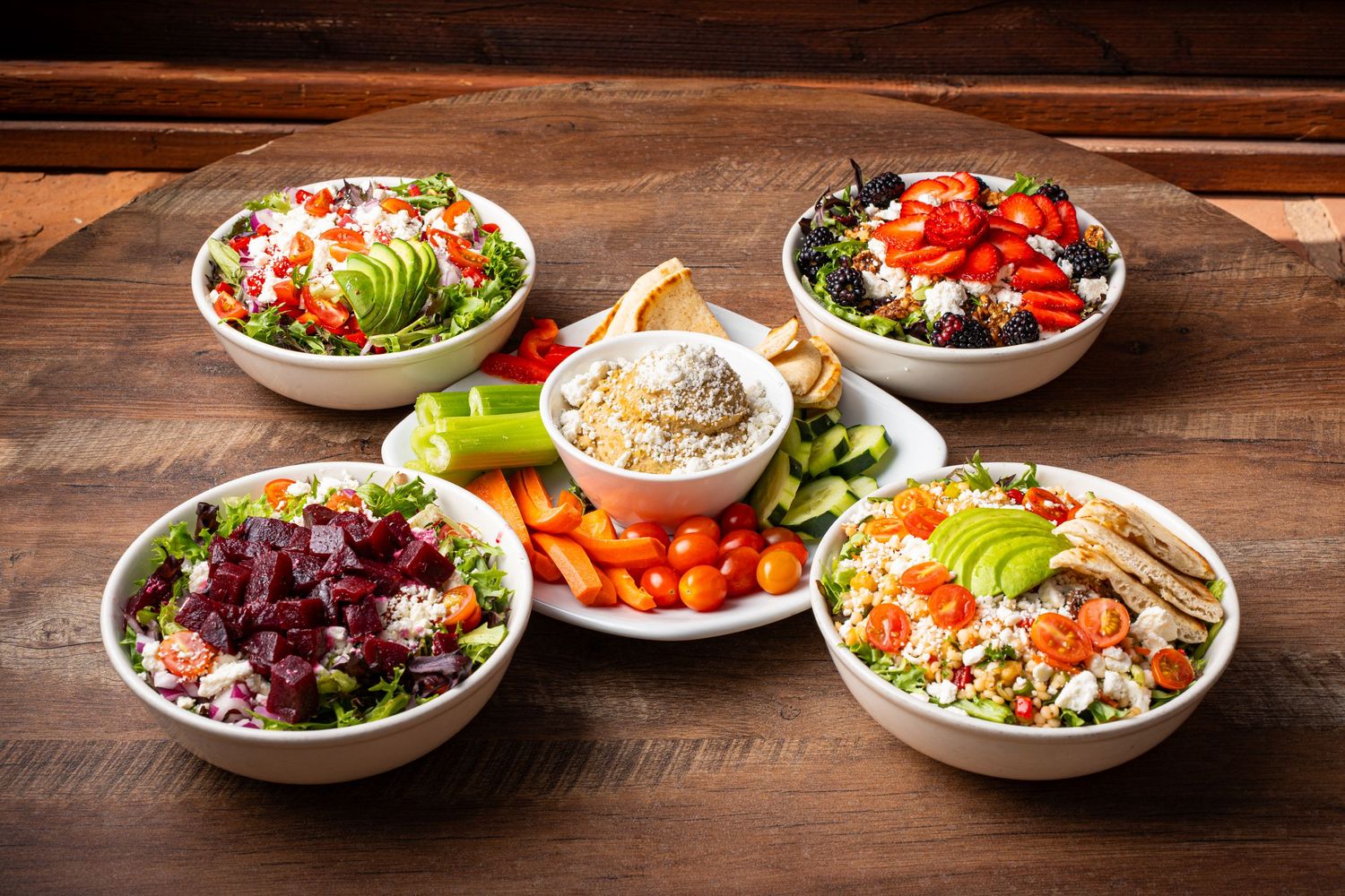 Five colorful salad bowls with fresh vegetables, avocado, beets, and grilled chicken on wooden table.