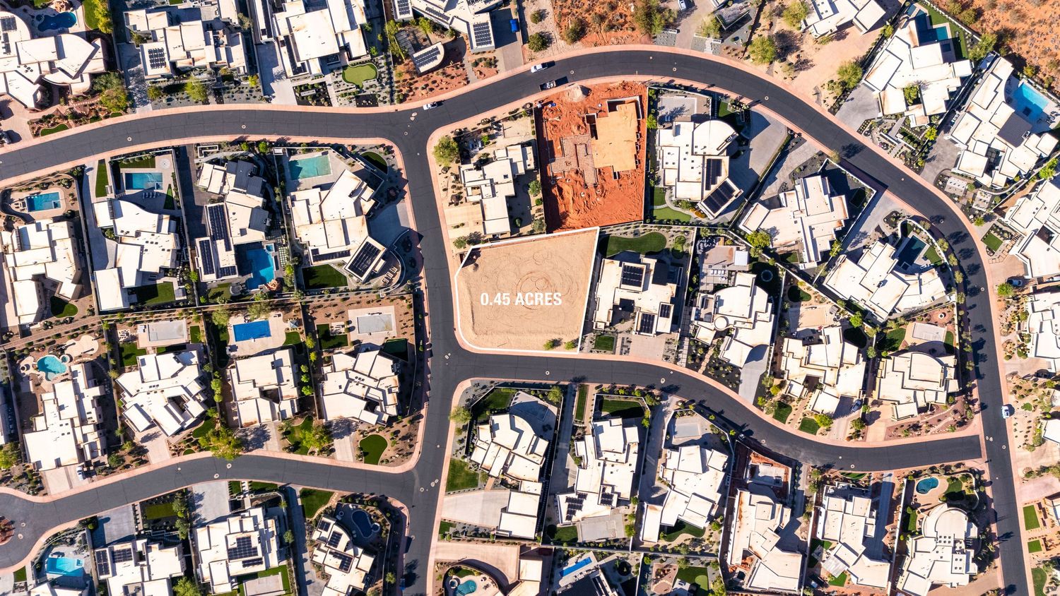 Aerial view of a residential neighborhood with an empty lot surrounded by luxury homes and winding streets in a desert setting.