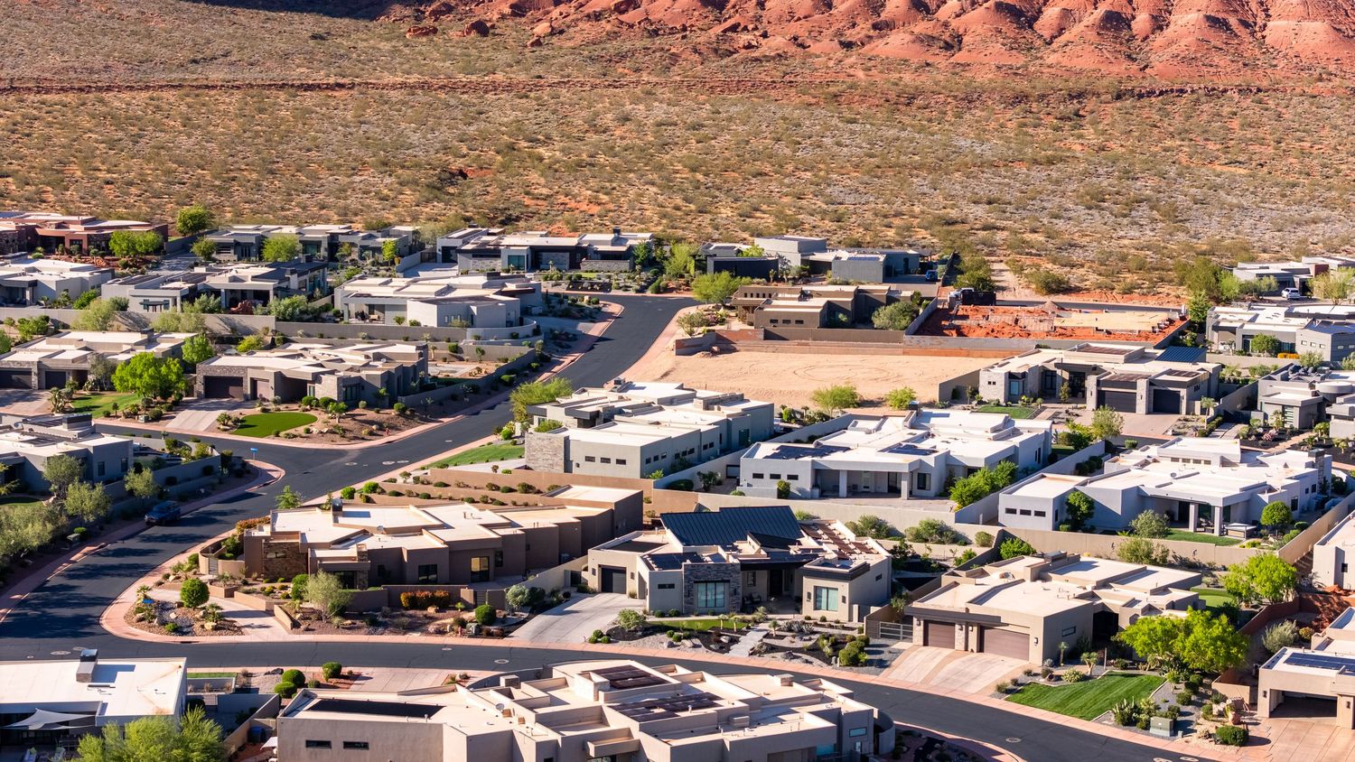Aerial view of a desert RV resort community with modern units, winding roads, and red rock mountains in the background.