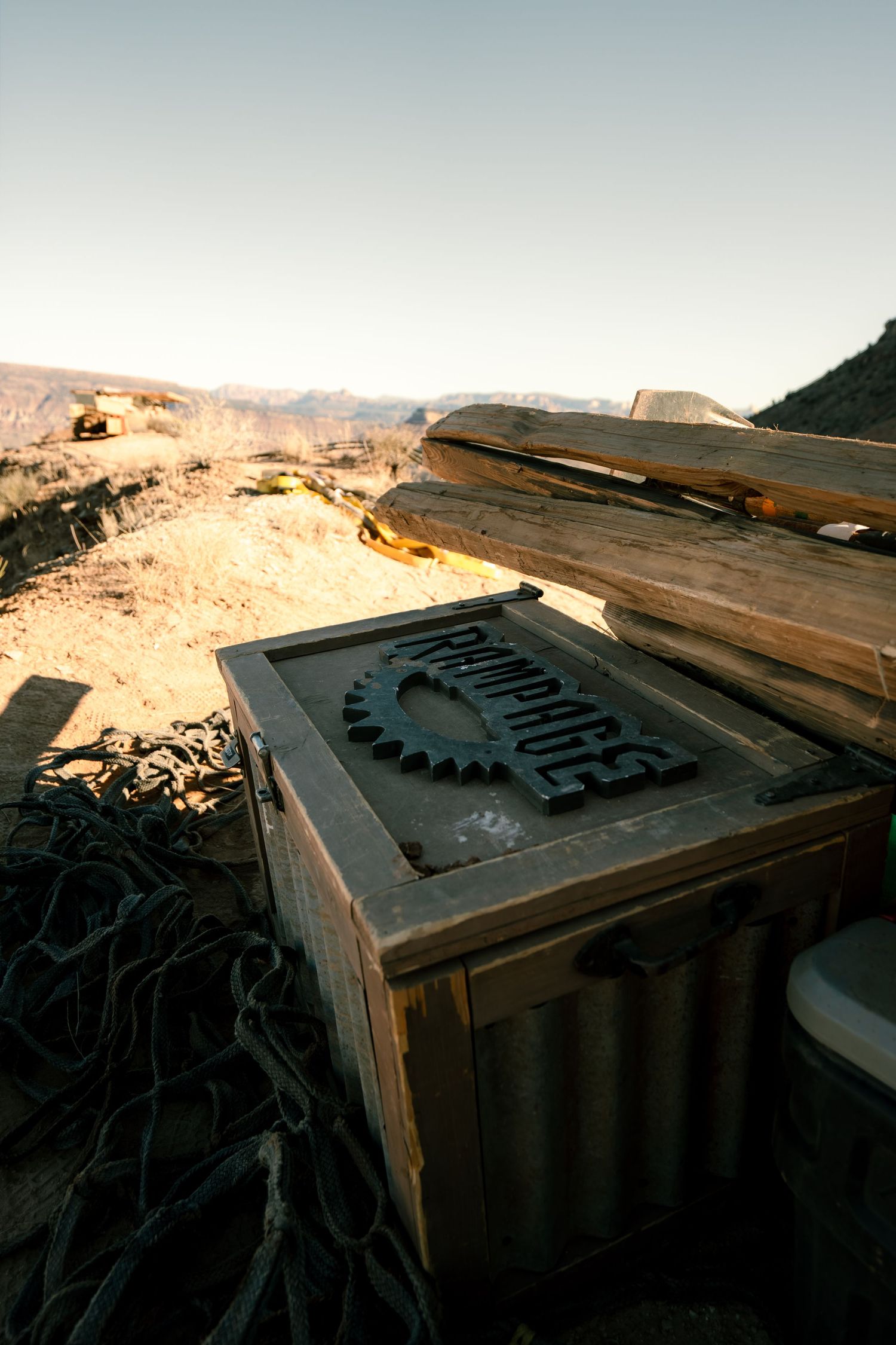 Wooden crate with Rampage logo sits on desert ridge surrounded by lumber and equipment at dusk.