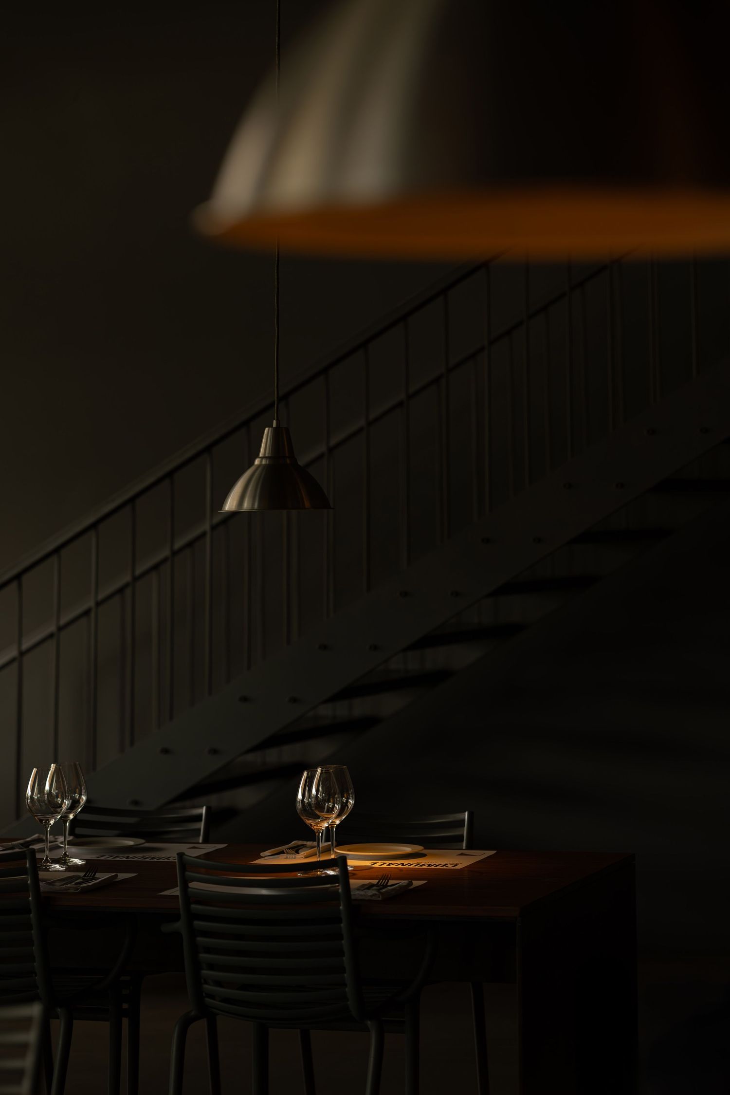 Dark moody restaurant Comunale interior with wine glasses on table and pendant lamp casting dramatic shadows.