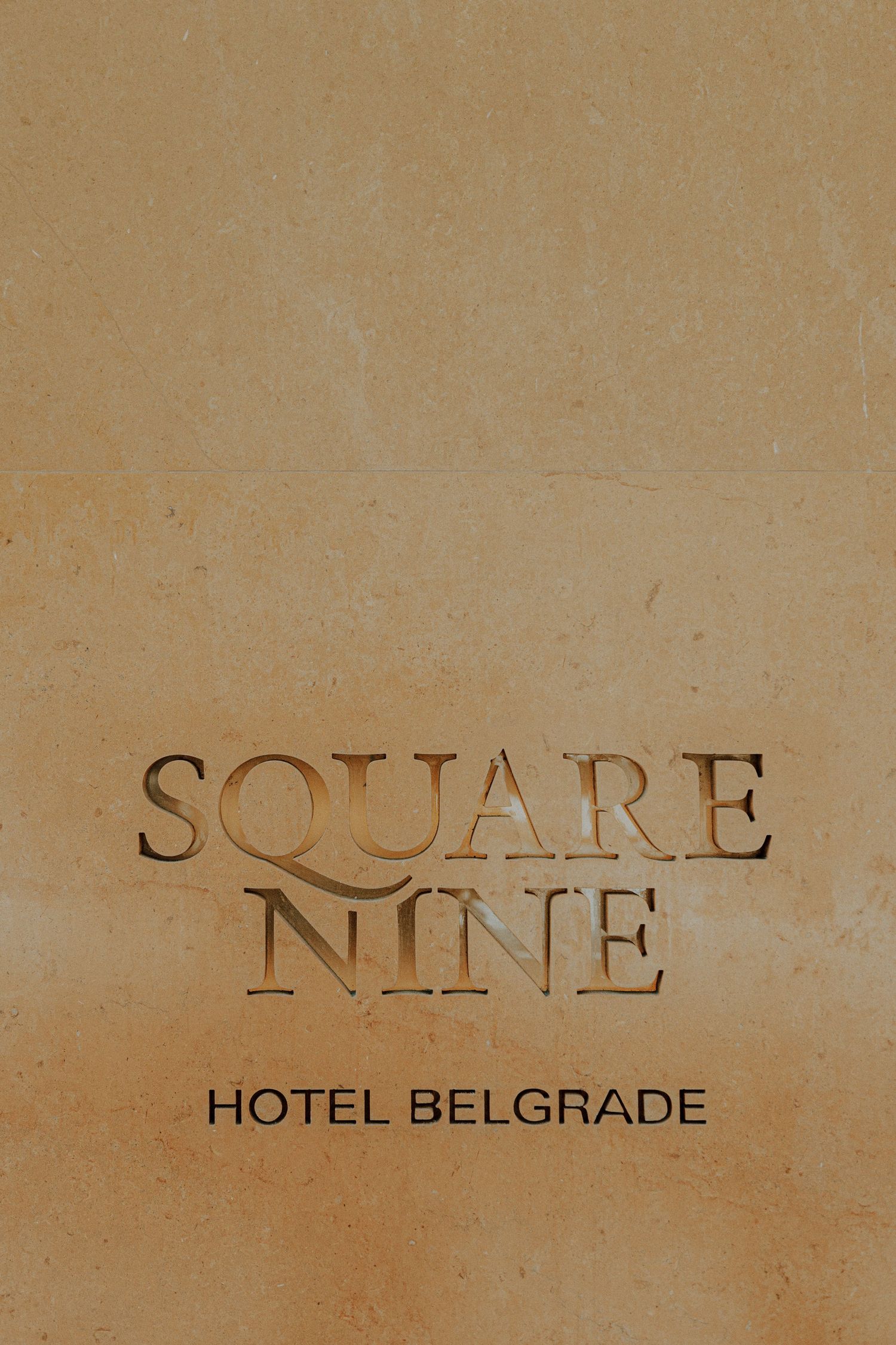 Square Nine Hotel Belgrade sign engraved in beige stone wall with elegant serif typography.