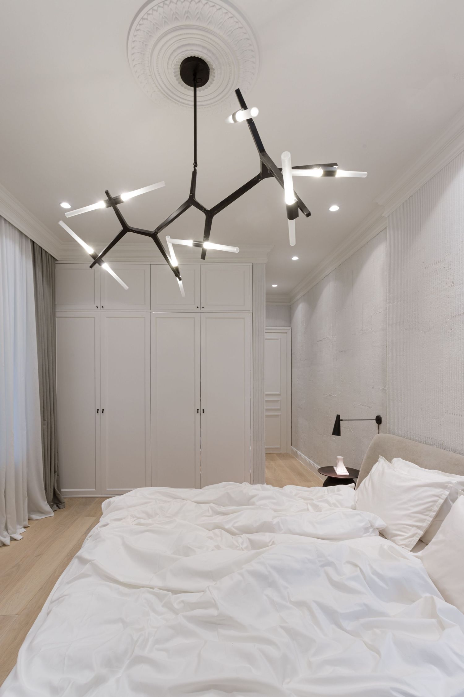Modern white bedroom with geometric black pendant lights and built-in storage cabinets featuring minimalist design by Vedrana Markovic.