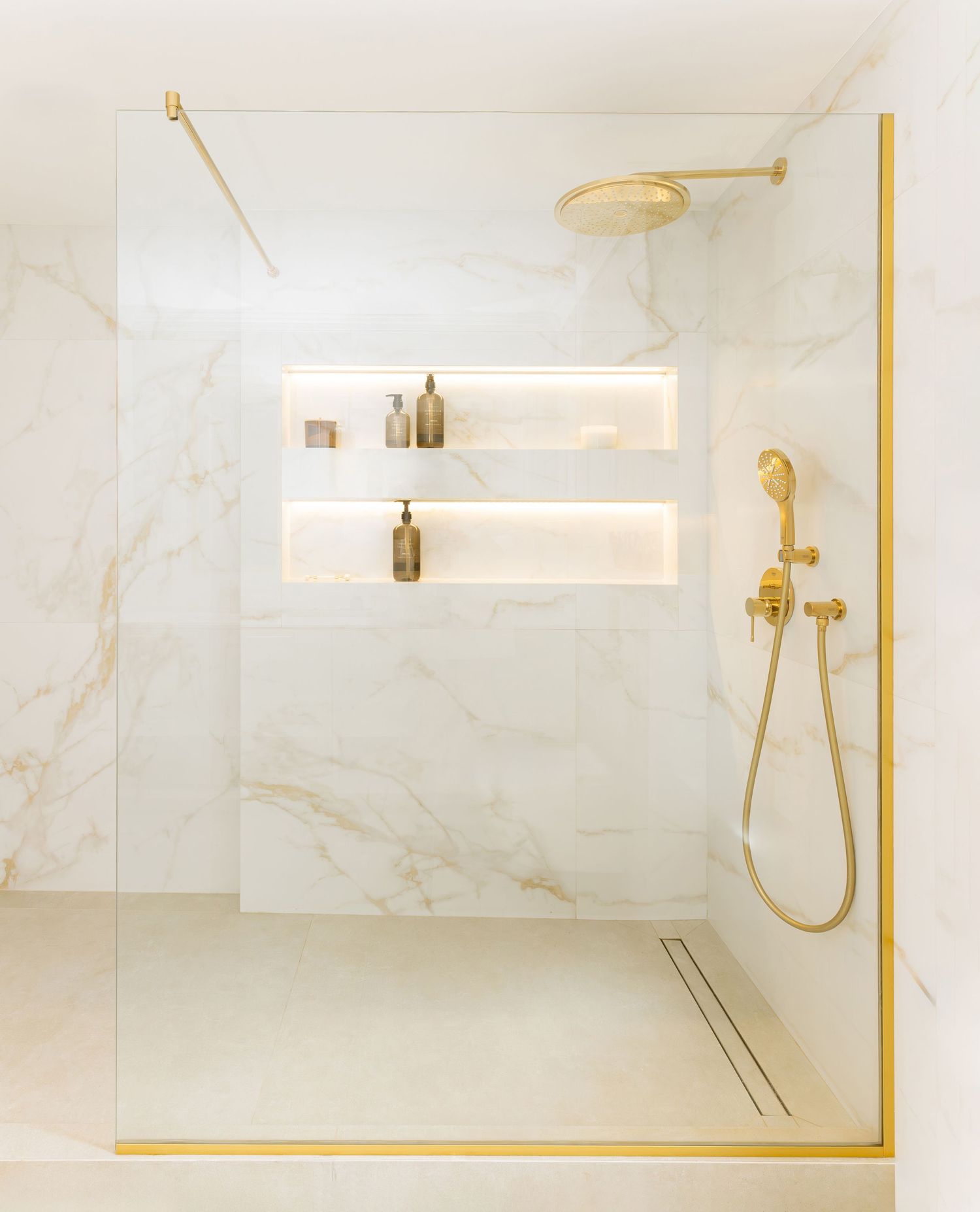 Bathroom interior with marble walls, gold fixtures, and built-in shower niche featuring luxurious brushed brass hardware by Vedrana Markovic