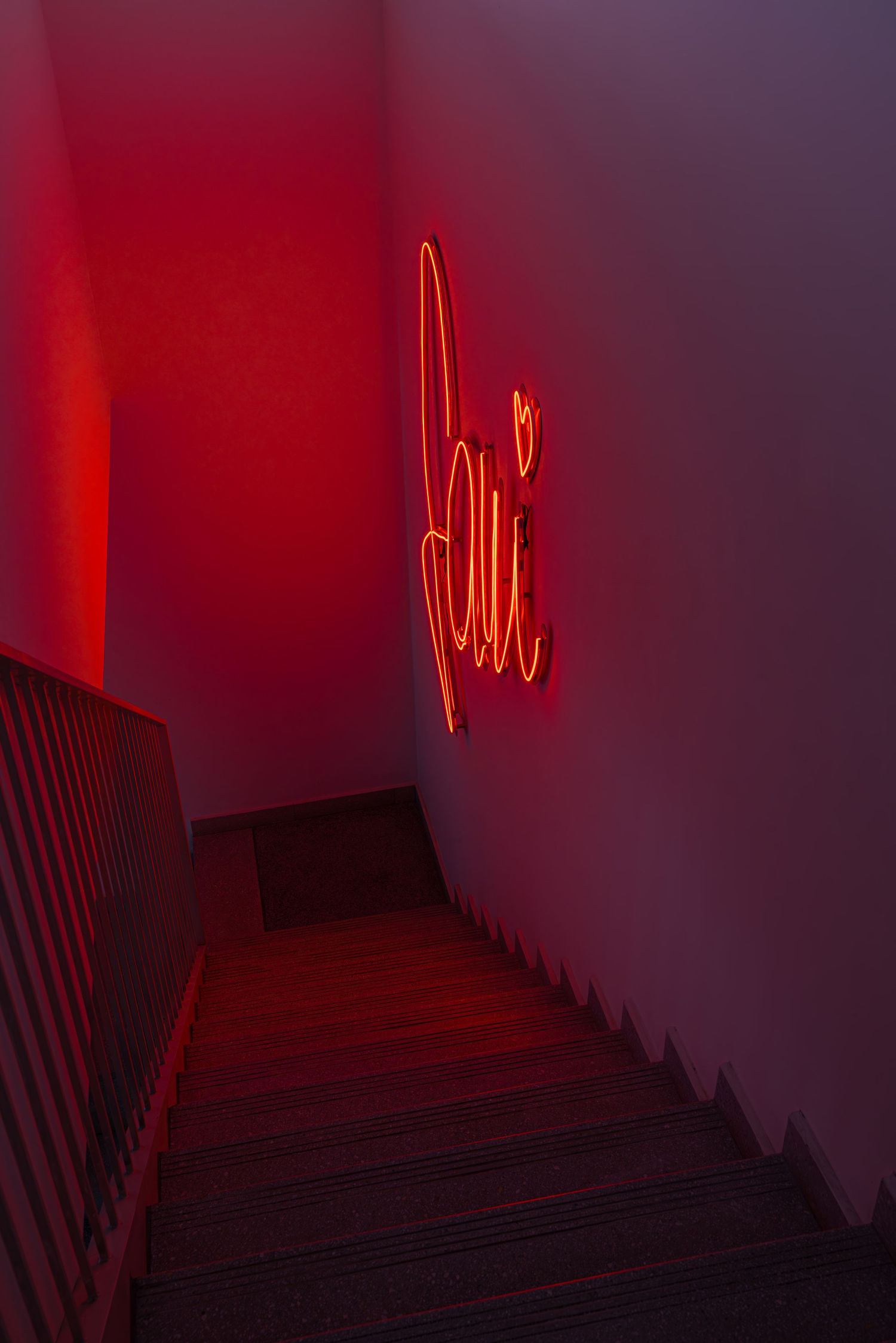 A dark stairwell illuminated by red neon lighting creates an eerie, moody atmosphere.