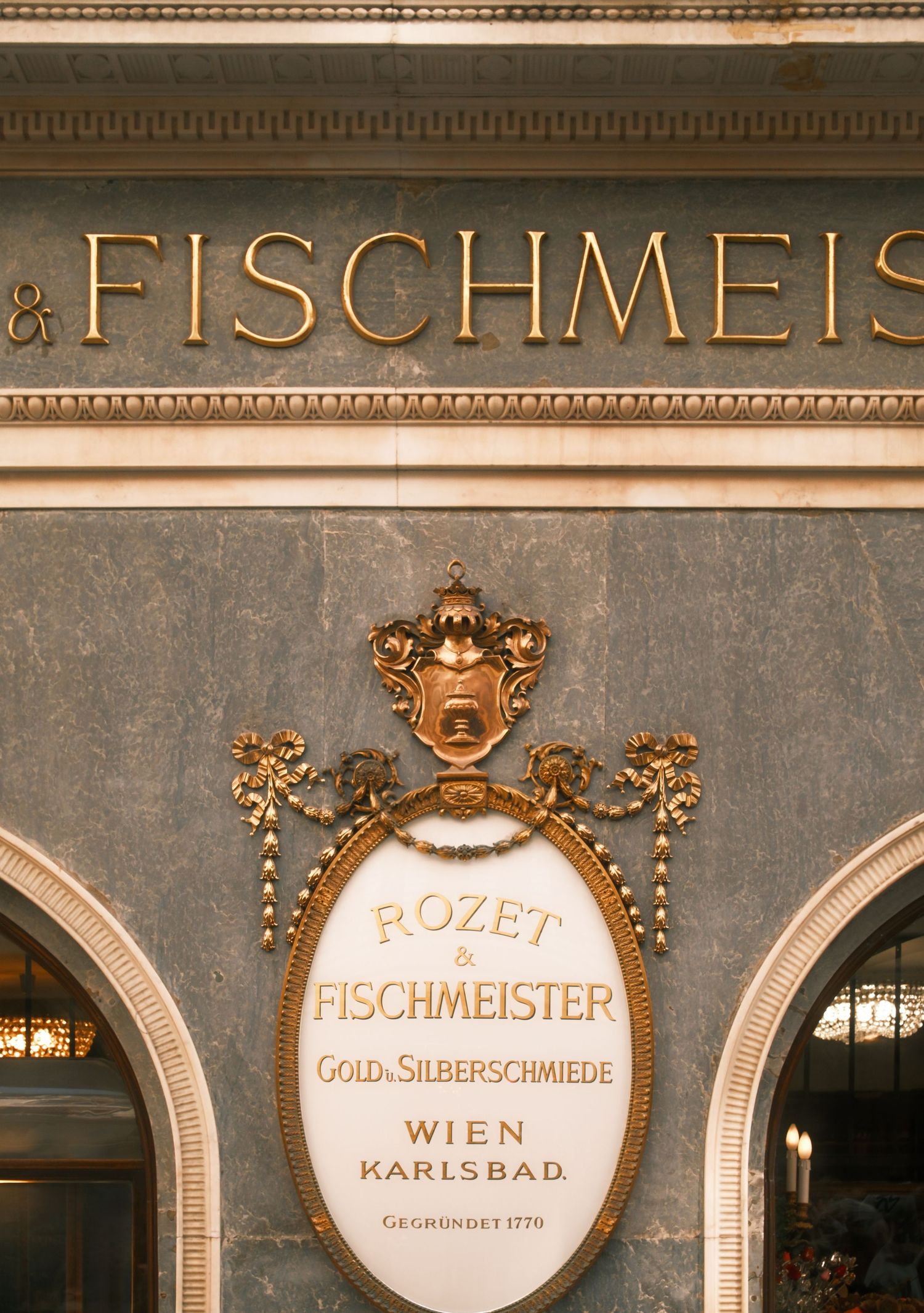 Vintage gold-lettered storefront signs for Fischmeister jewelers and goldsmiths in Vienna display elegant architectural details.