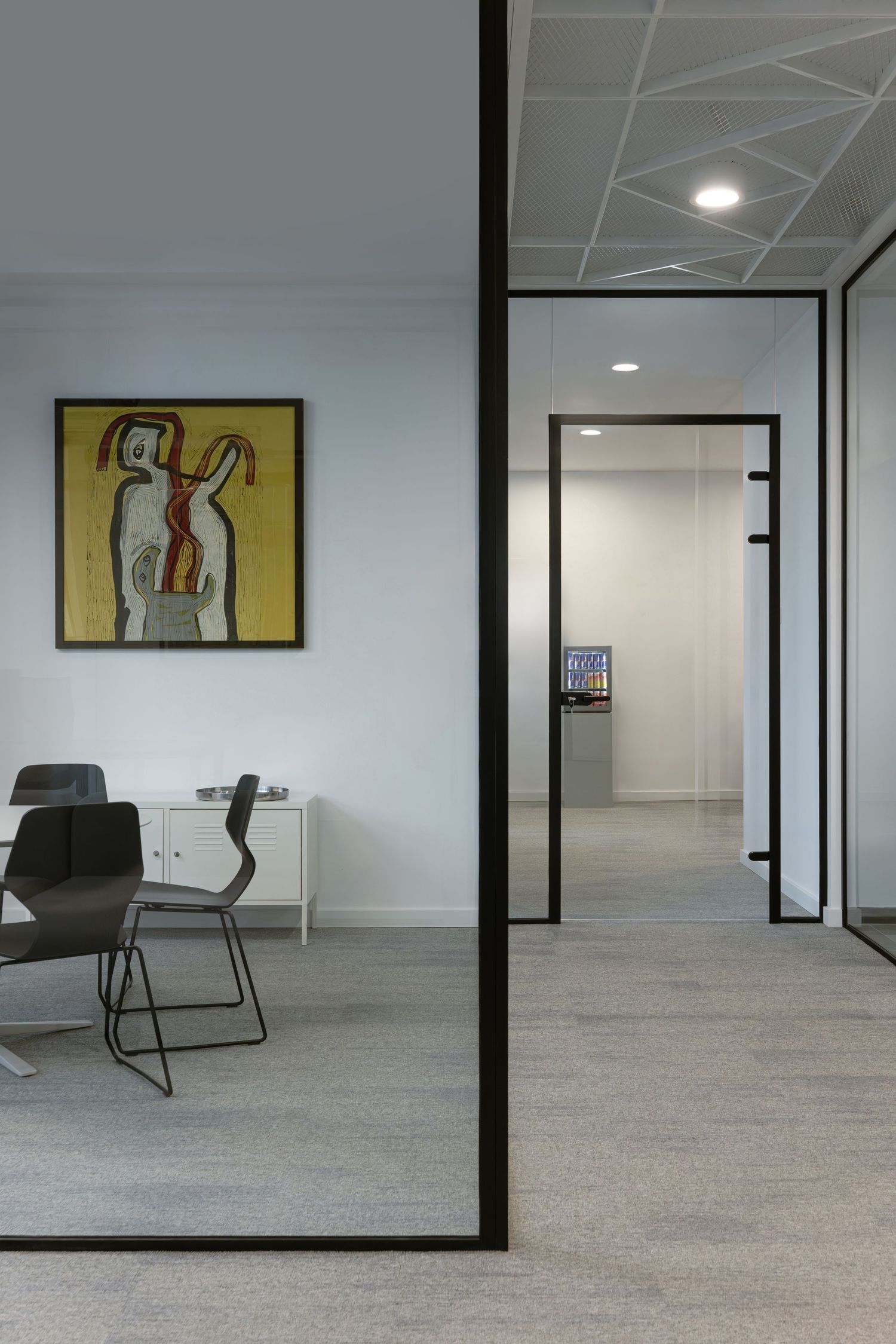 Modern office interior with gray carpet, white walls, and minimalist artwork featuring abstract designs on display.