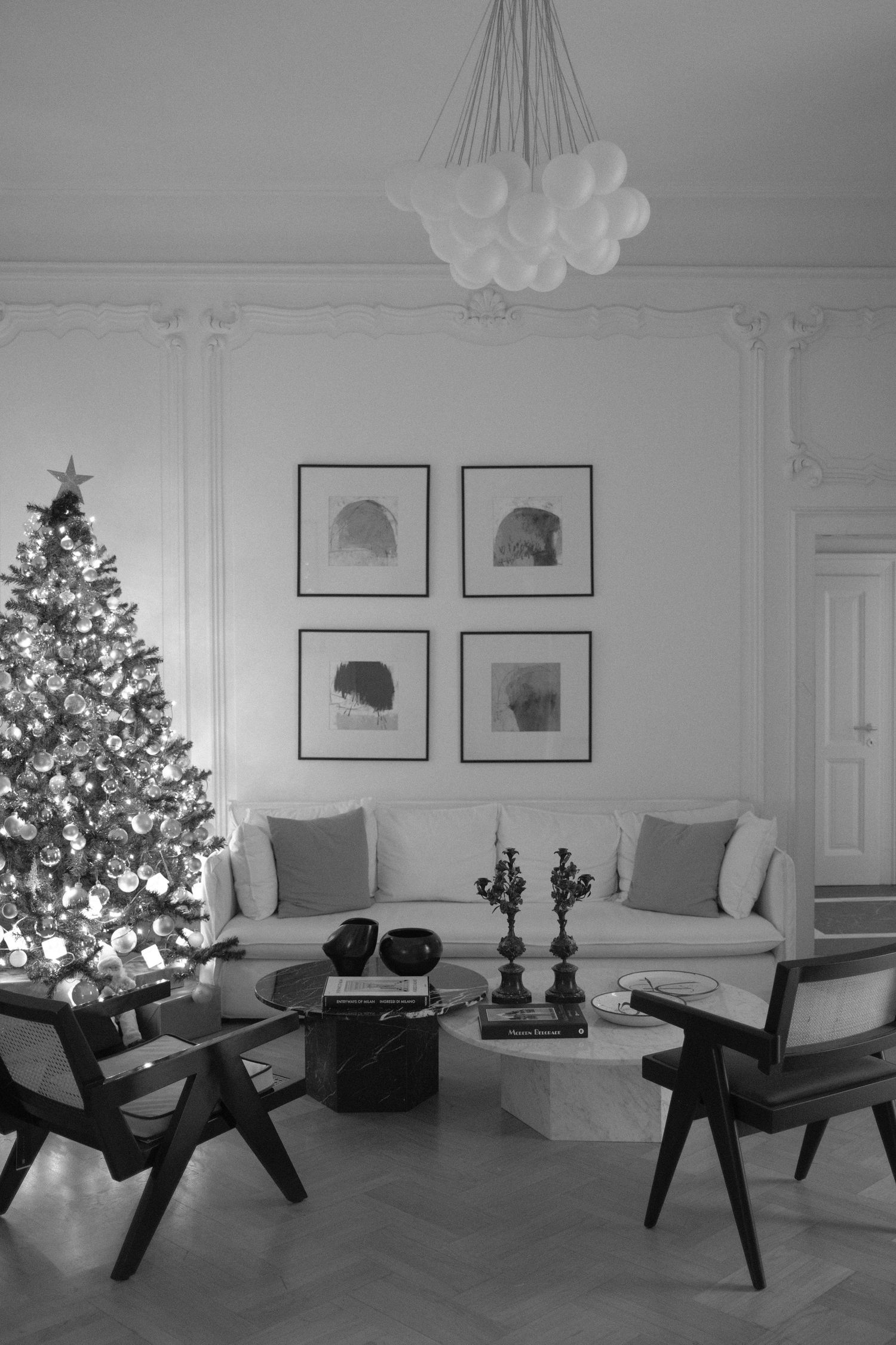 Black and white panoramic view of a modern living room with Christmas tree, grey seating, and framed wall art.