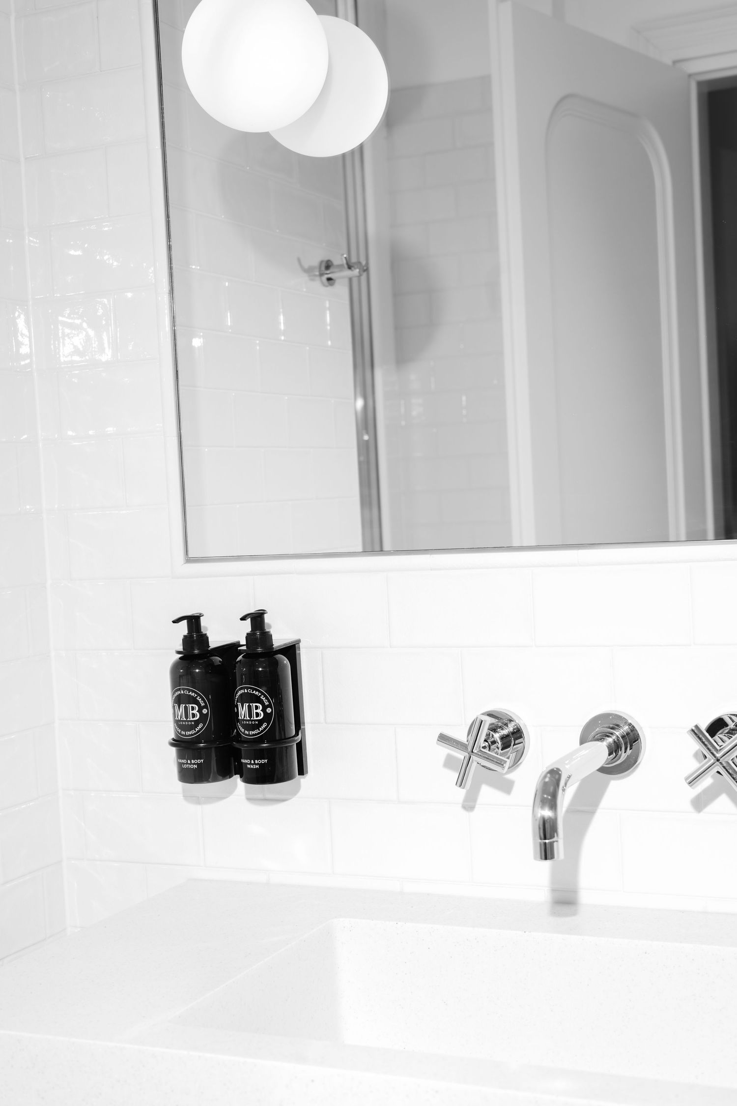 Modern bathroom vanity with black toiletry bottles and round pendant lights reflecting in a sleek white mirror in Hotel Fermai Split