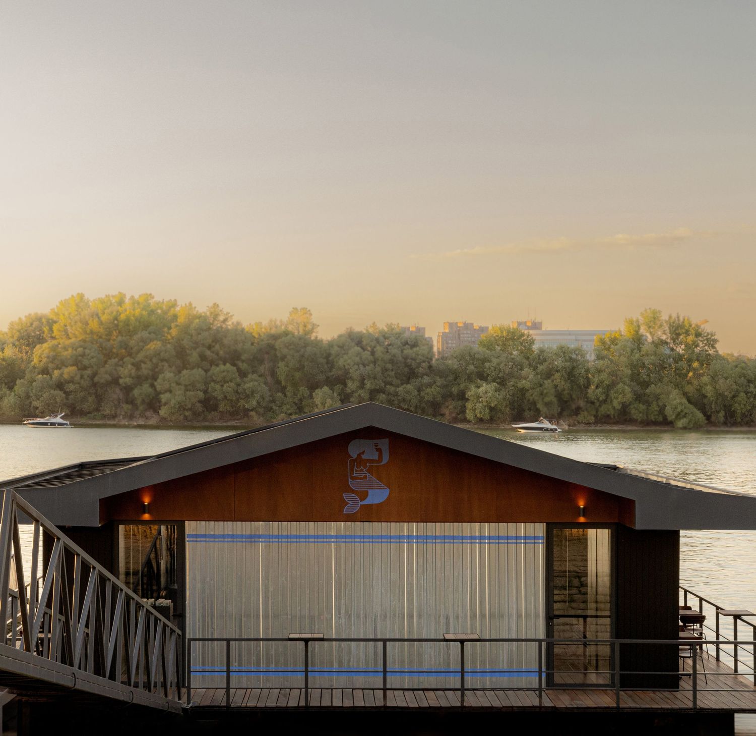 Panoramic sunset view of a lakeside dock with wooden buildings and trees silhouetted against an orange sky.