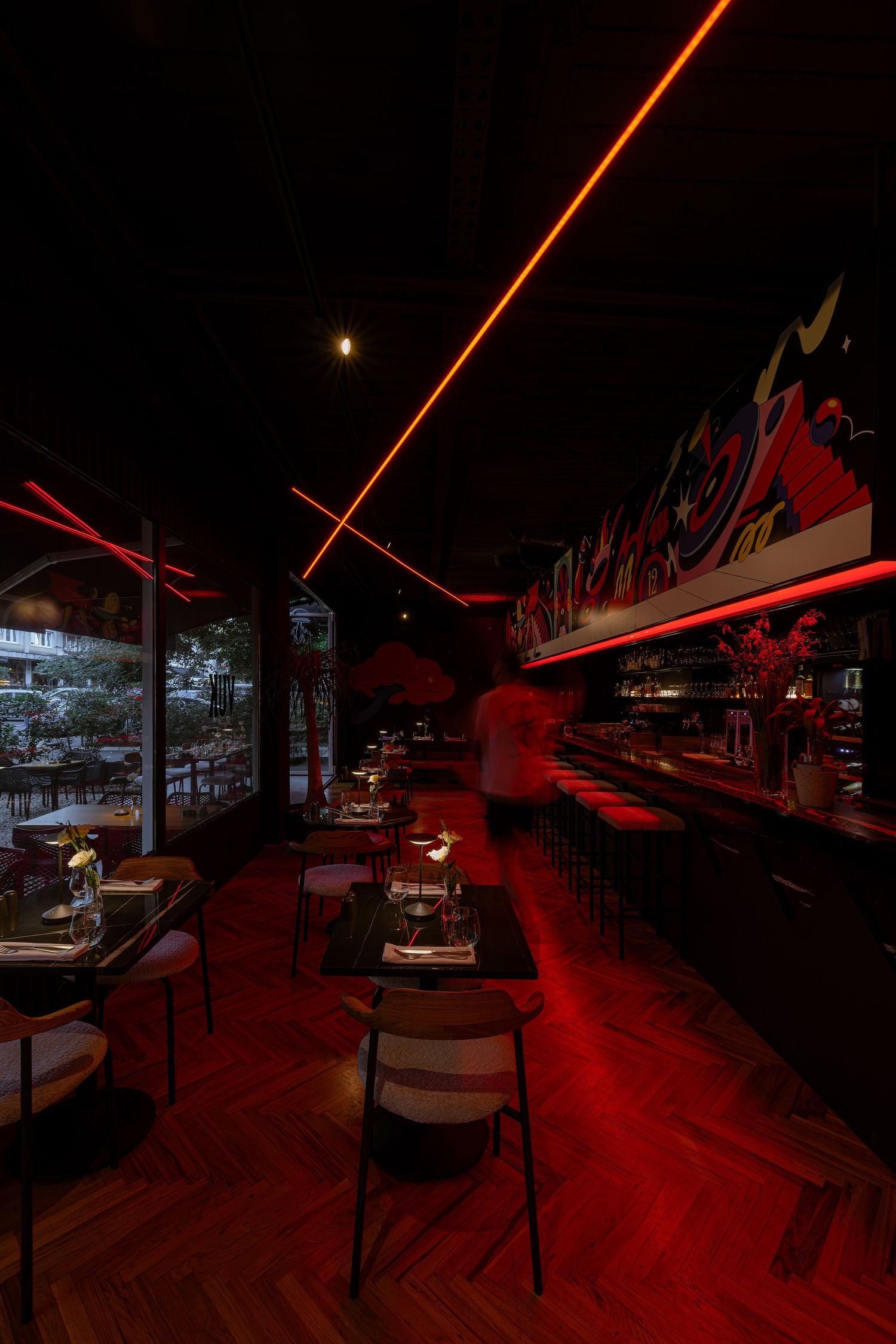 Modern restaurant interior with red ambient lighting and wooden flooring creates a dramatic nightclub atmosphere.