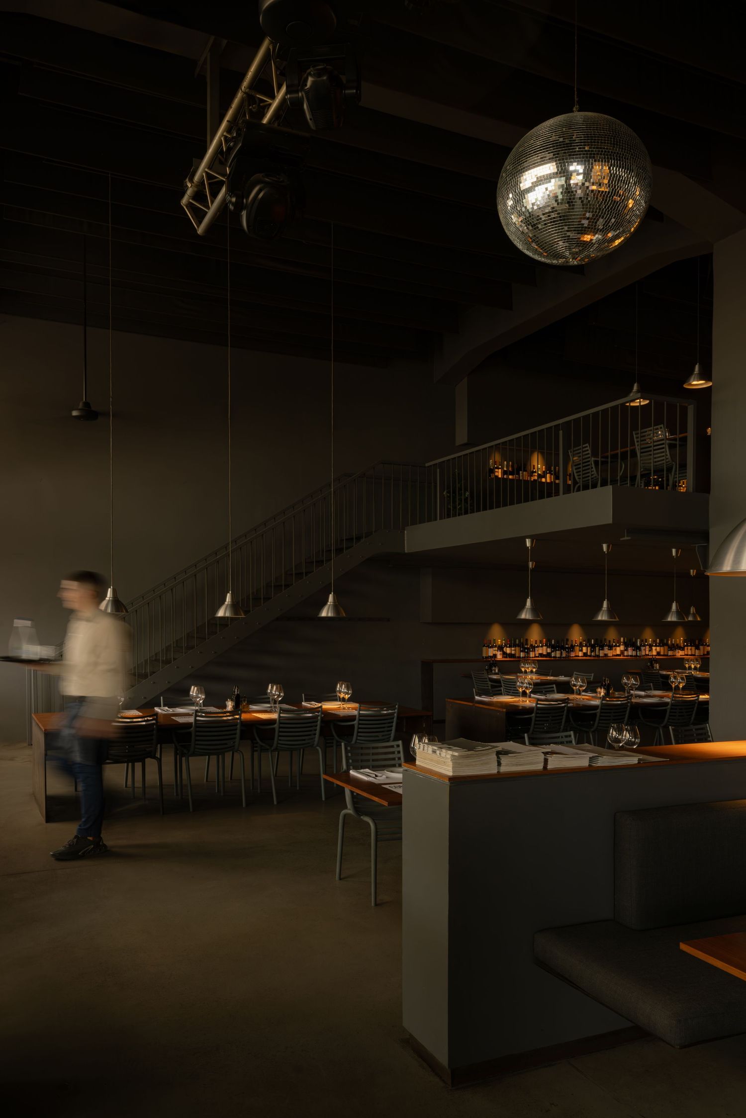 Dark minimalist Comunale restaurant in Belgrade, interior with pendant lighting and wooden tables creating a moody atmosphere.