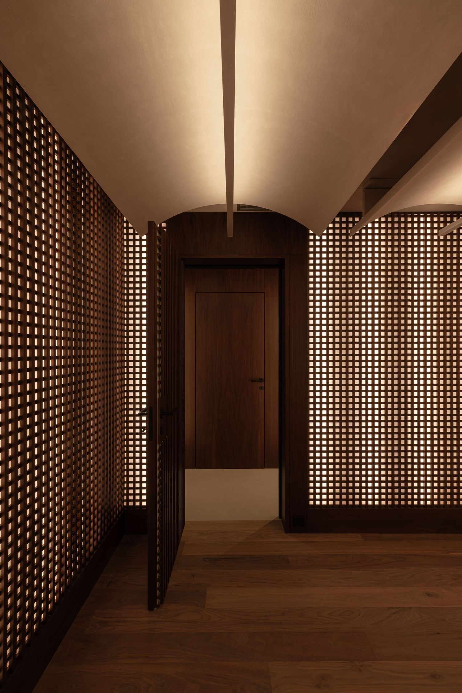 Modern interior hallway with geometric perforated wall panels creating dramatic lighting patterns on wooden flooring by Studio Fluid.