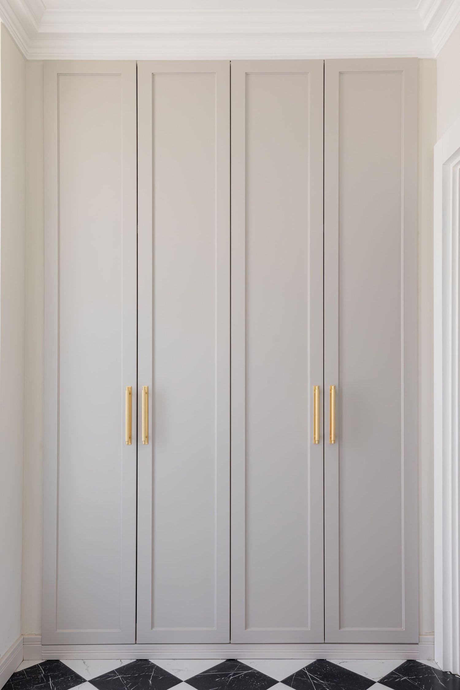 Modern built-in closet with light gray shaker-style doors and brass handles creates elegant bedroom storage solution by Vedrana Markovic.