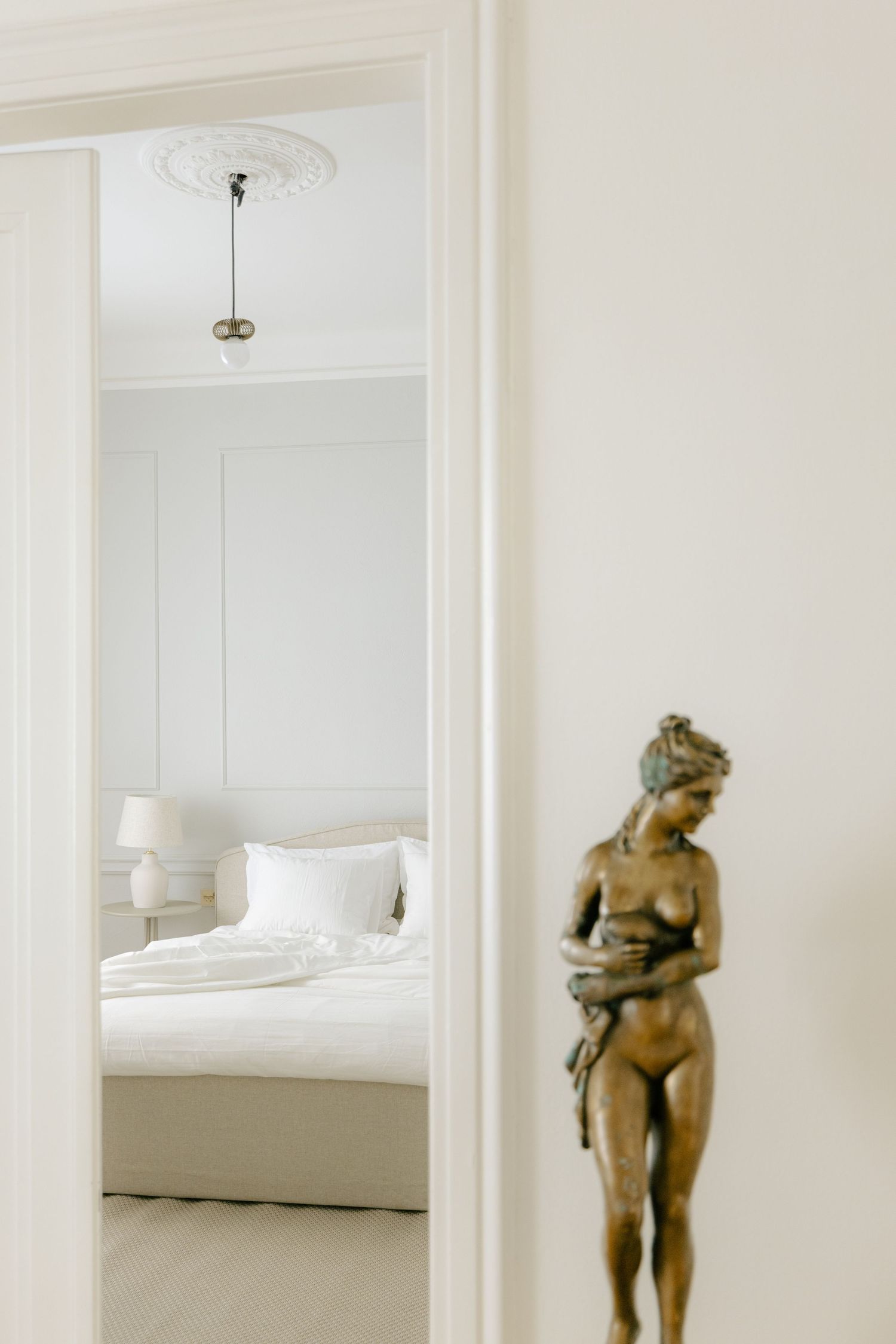 Elegant white bedroom viewed through doorway with bronze female statue door handle in foreground.