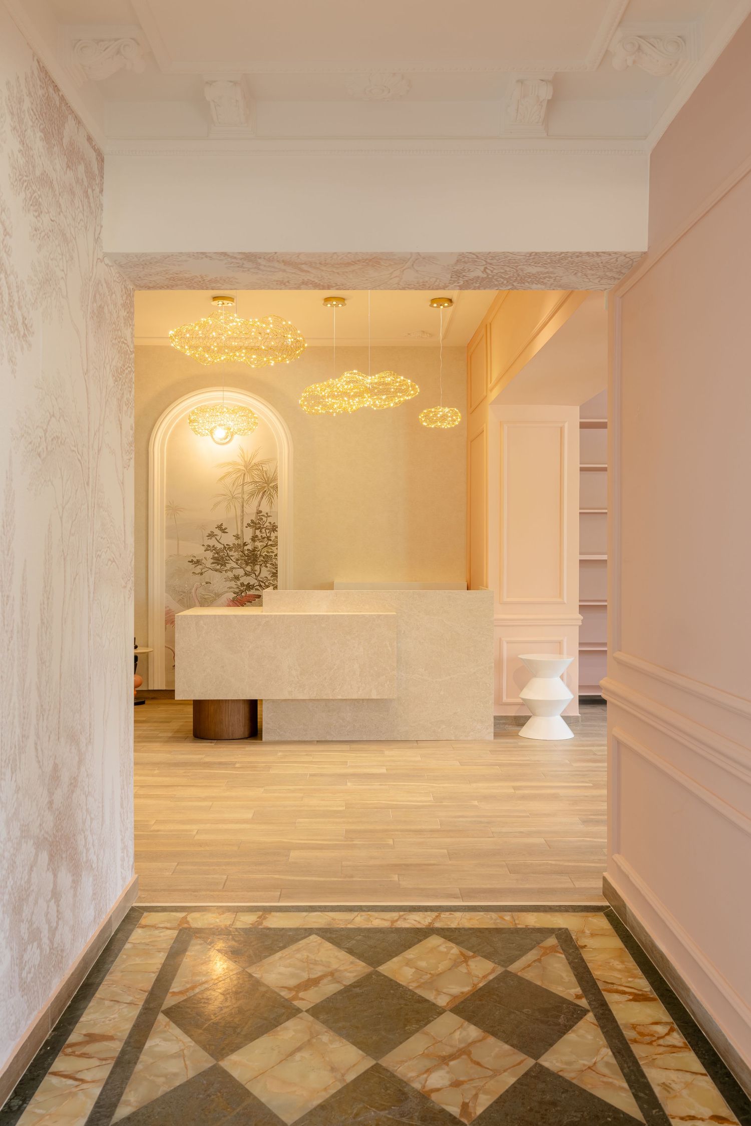 Elegant reception area with marble desk, cloud-shaped gold chandeliers, arched wall, and checkered marble floor entrance.