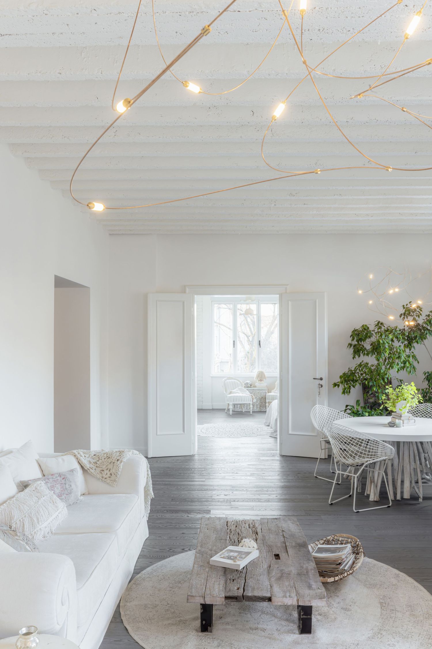 Modern white studio space with string lights, rustic wood floors, featuring Knoll Diamond chair.